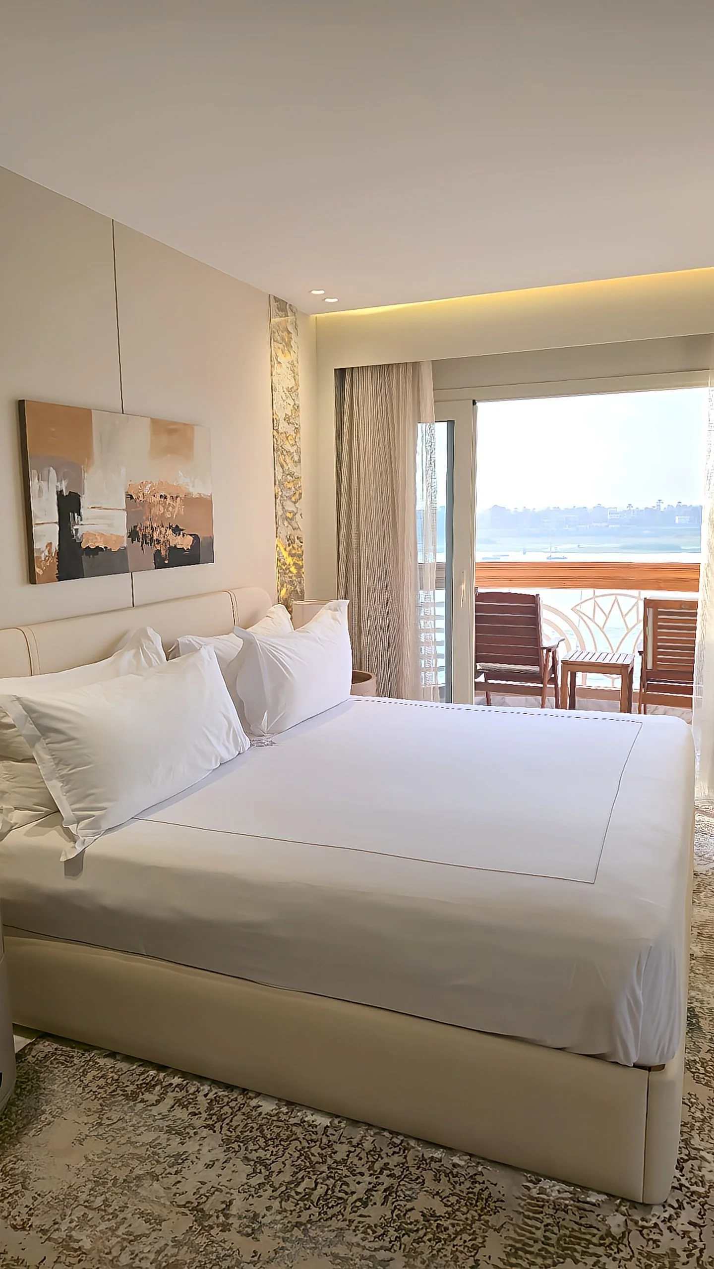 Bright king bedroom opening to a private balcony overlooking the Nile River at sunset, Sonesta St. George Hotel Luxor.