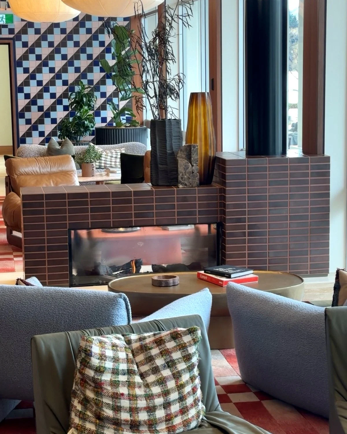 Contemporary hotel lounge featuring a tiled fireplace, comfortable sofas, patterned cushions, and modern artwork