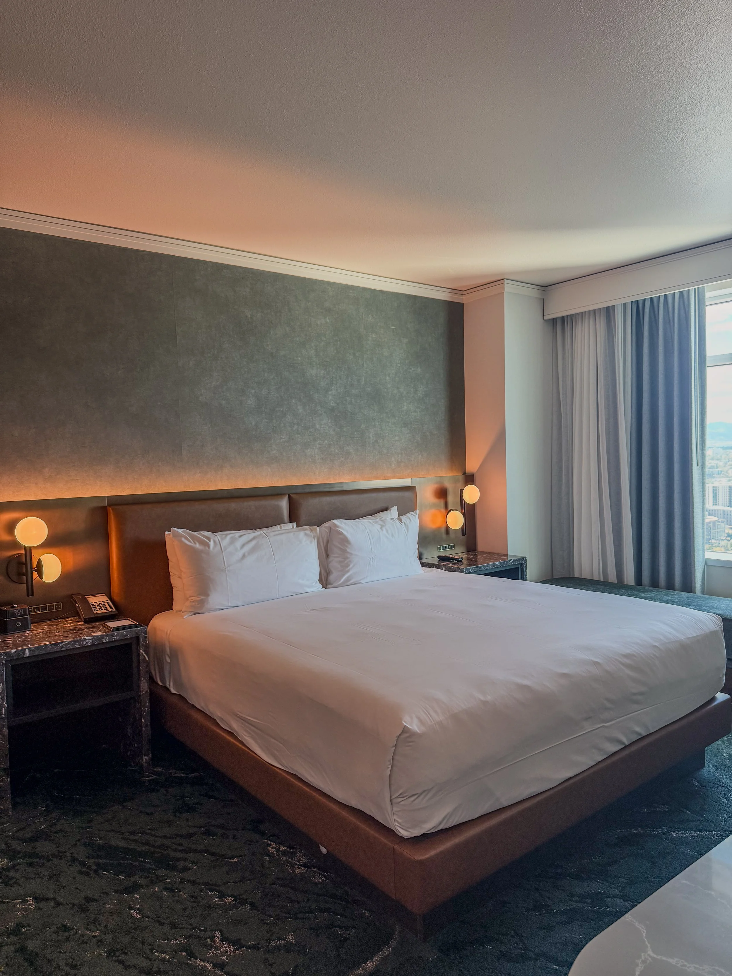 Modern hotel bedroom with a king-size bed, marble bedside tables, and large windows overlooking Denver