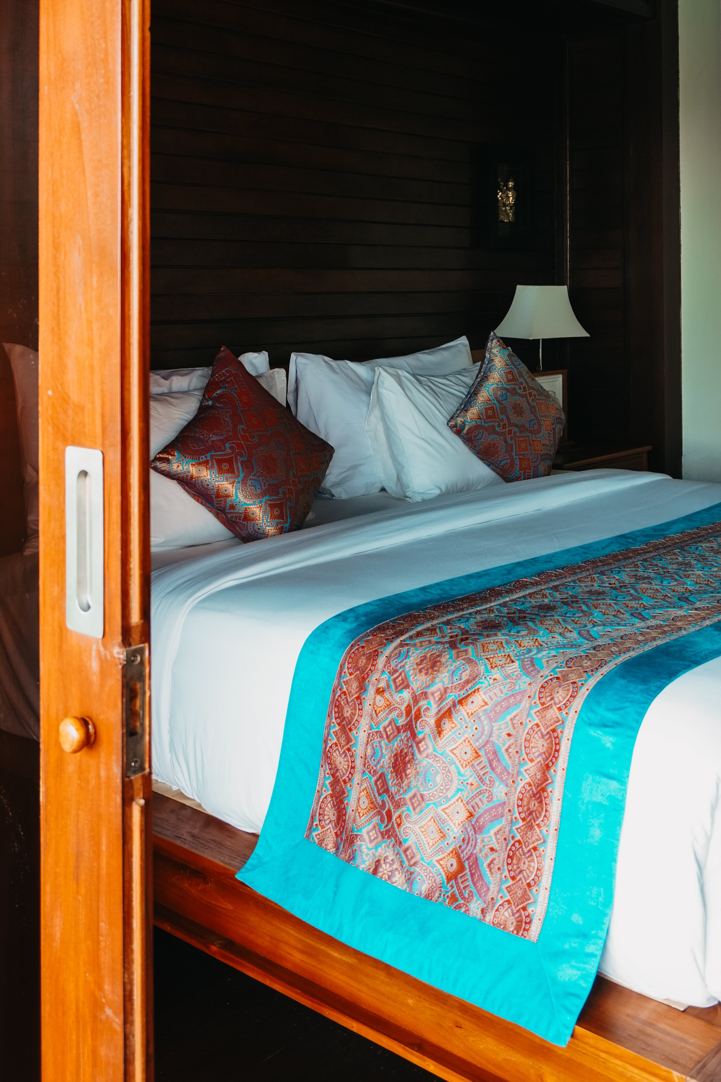 Luxury wooden bedroom with king bed, decorative pillows, and tropical interior design at Pramana Nusa Ceningan Resort Bali