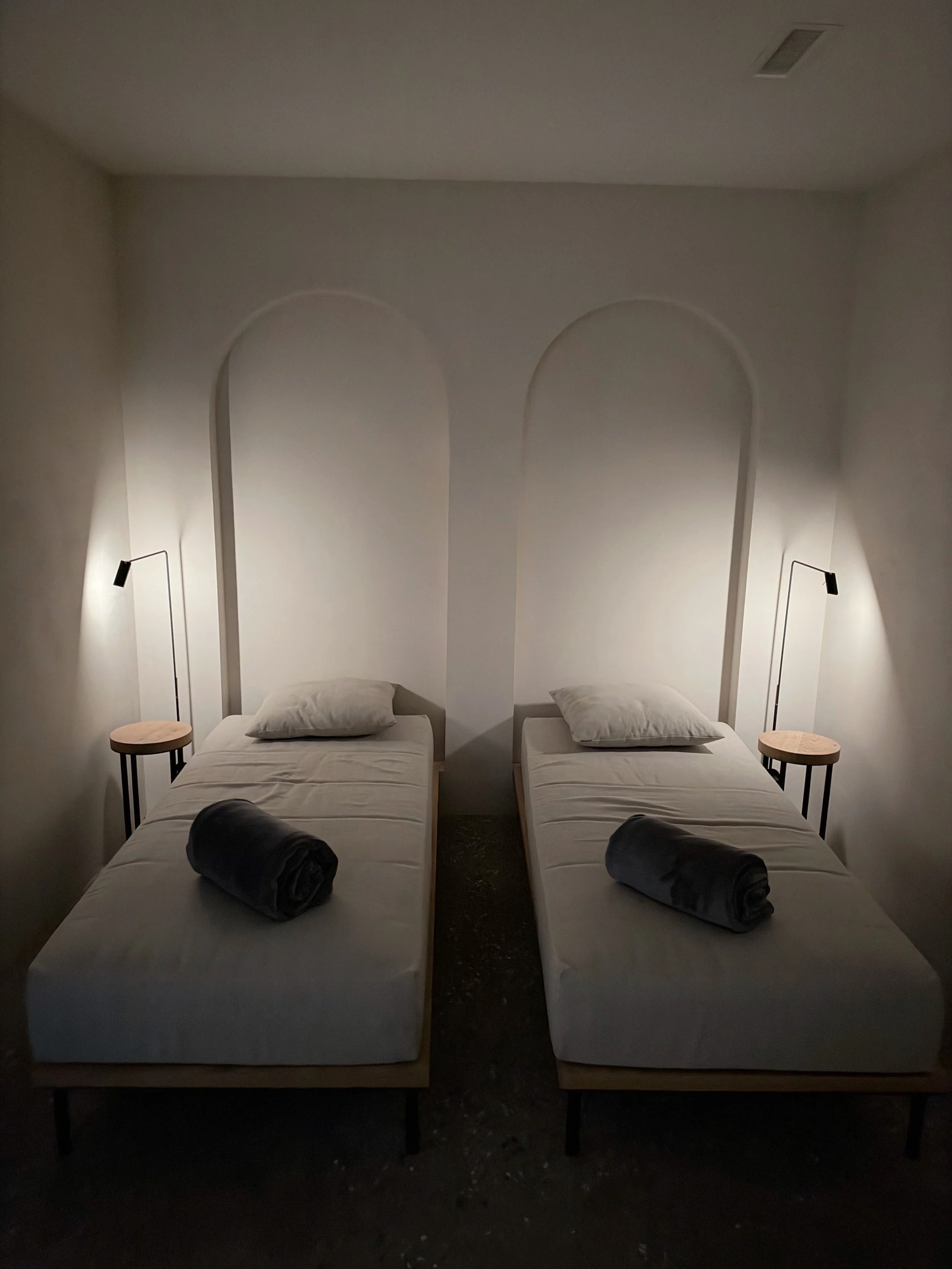 Peaceful relaxation room with two treatment beds, soft lighting, and minimalist arched wall details