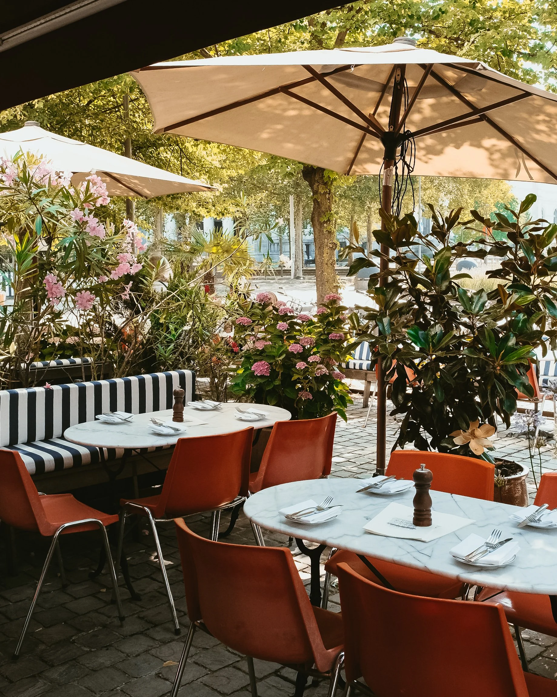 Outdoor terrace framed by lush greenery, marble tables, and vibrant seating beside the city square