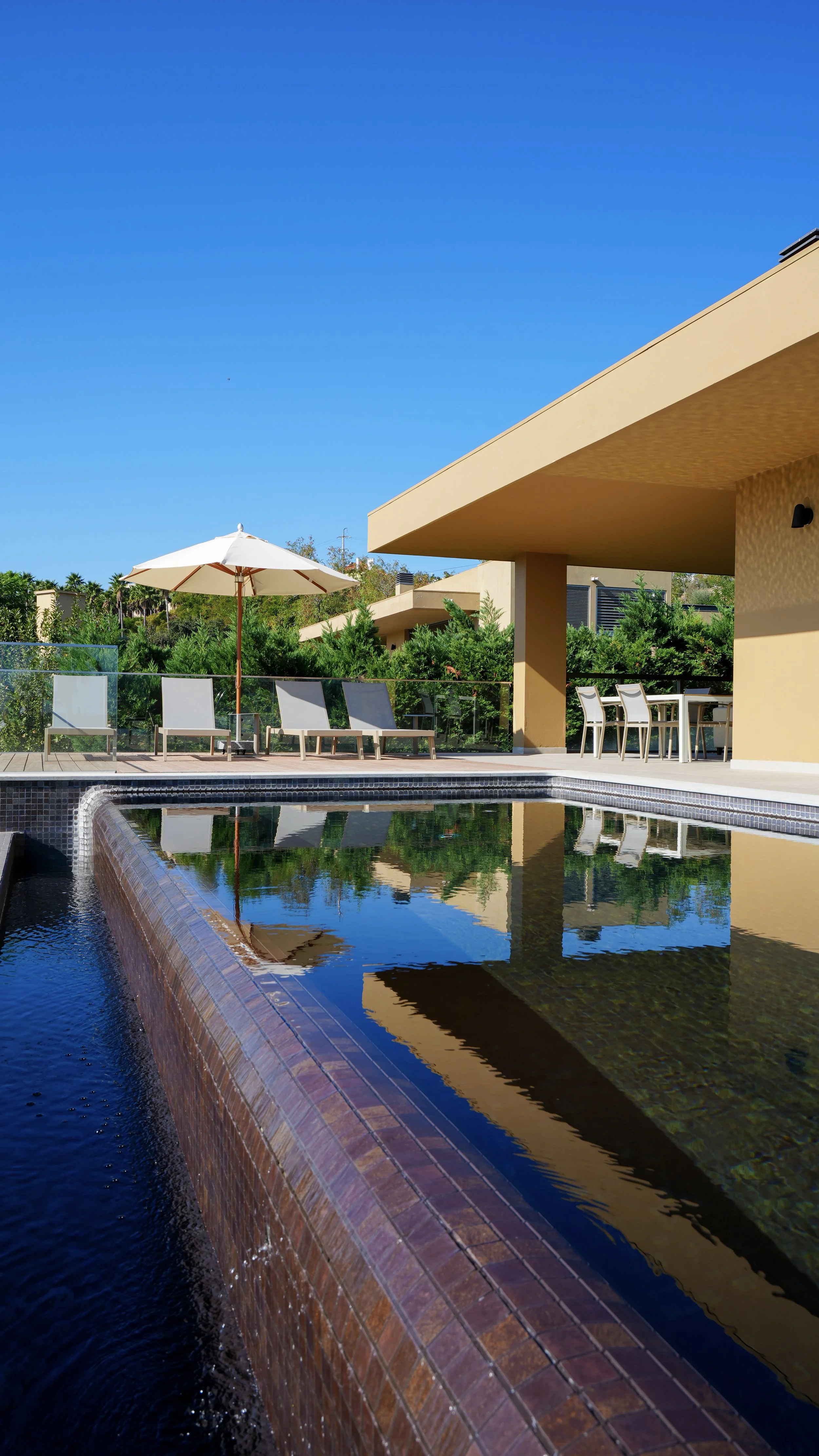 Elevated outdoor swimming pool with cascading water, sun loungers, and a shaded terrace