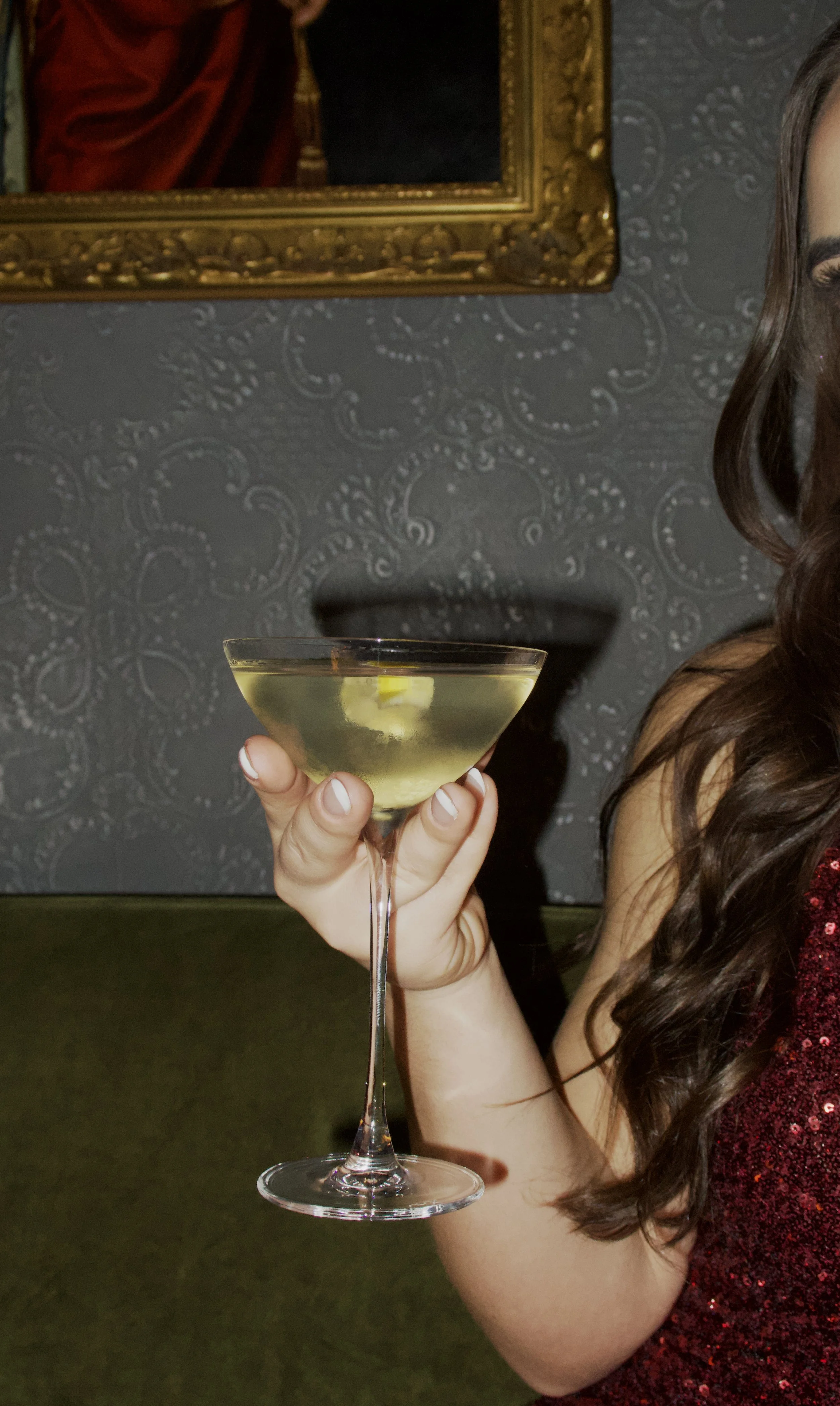 Close-up of a classic cocktail in a coupe glass against patterned wallpaper and framed artwork, Victoria Palace Hotel – Paris, France.