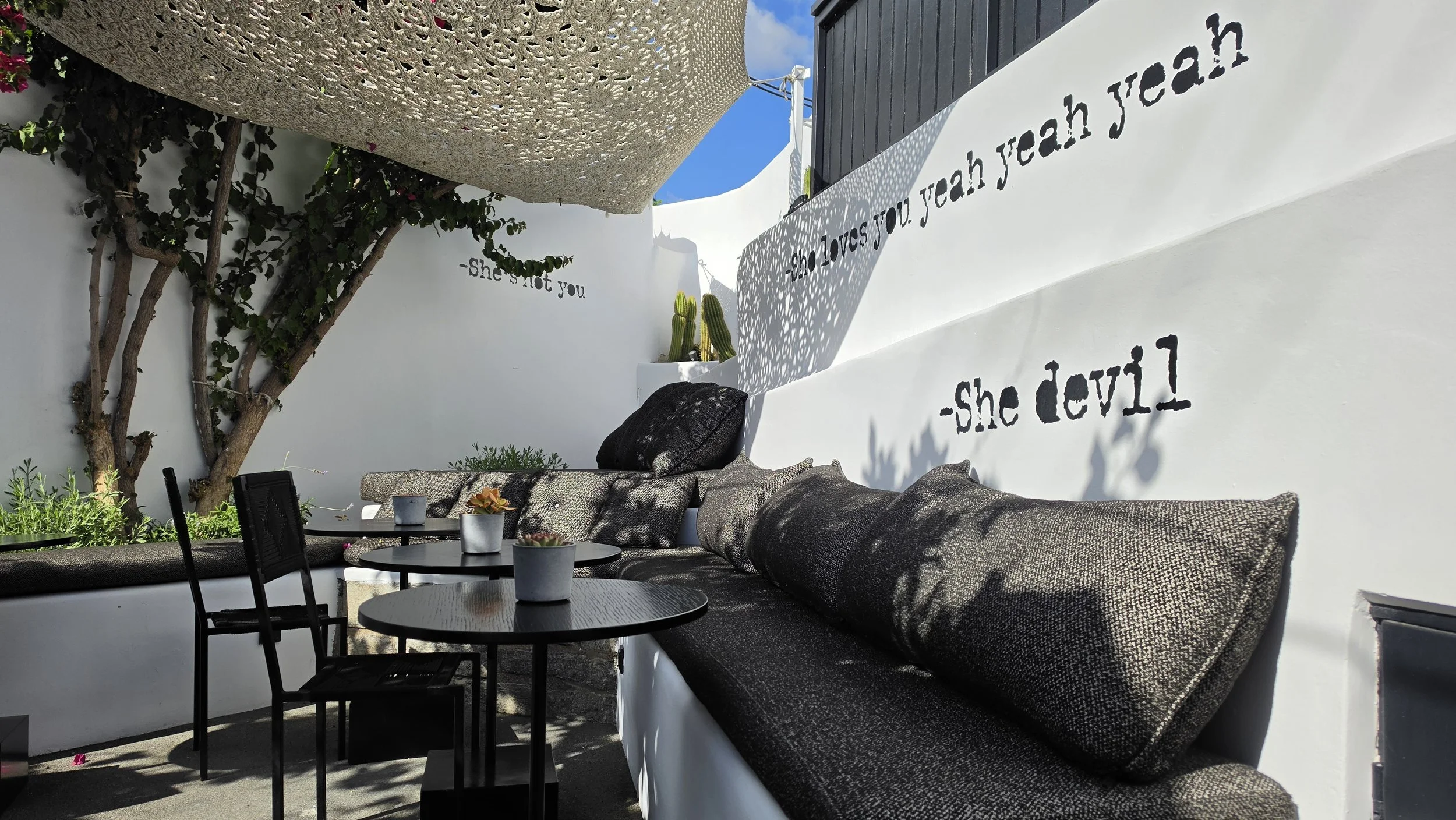 Sunlit courtyard terrace with statement typography and lounge seating at She Mykonos Hotel in Mykonos, Greece