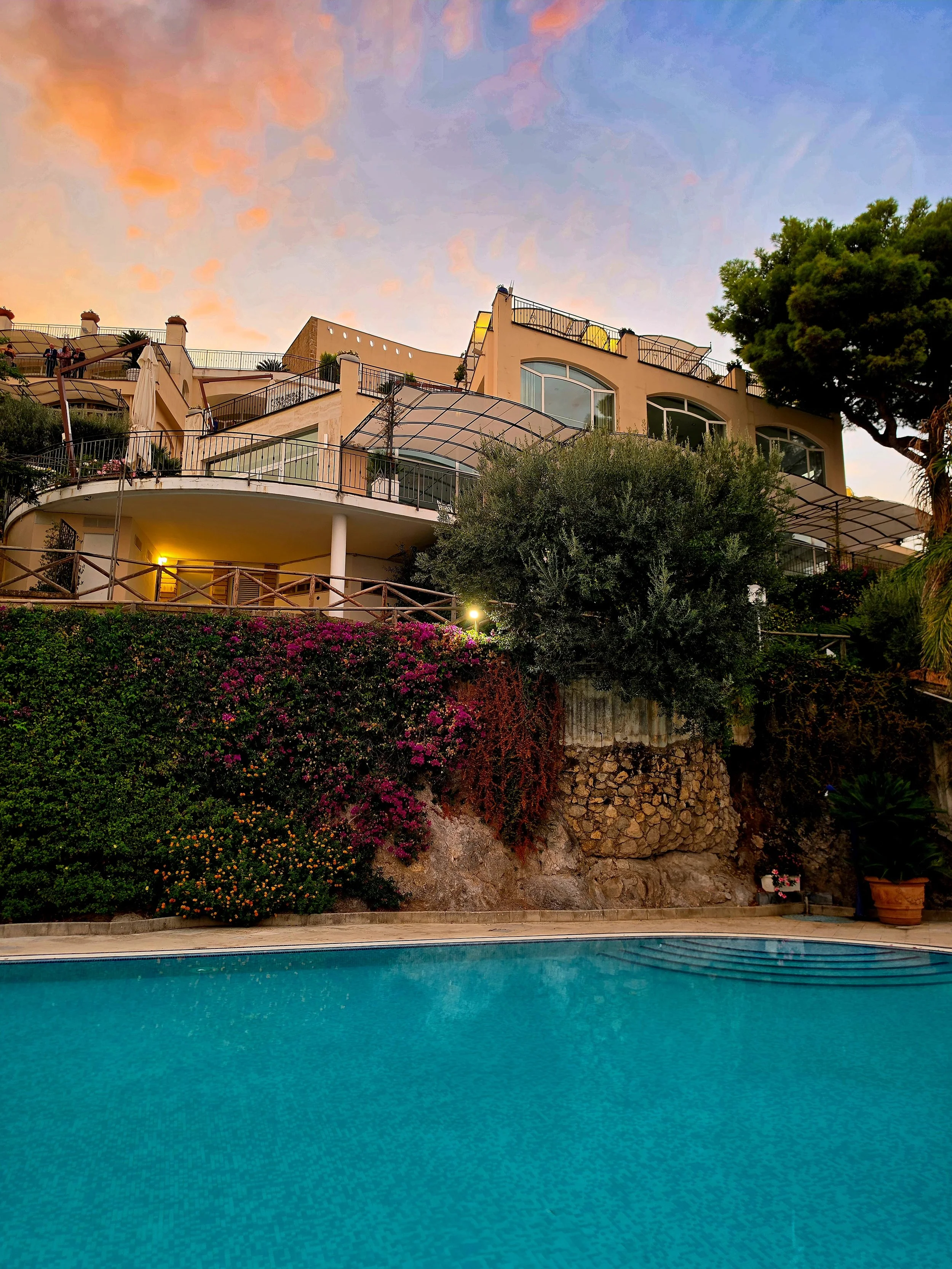 Outdoor swimming pool below the hillside hotel surrounded by lush Mediterranean gardens