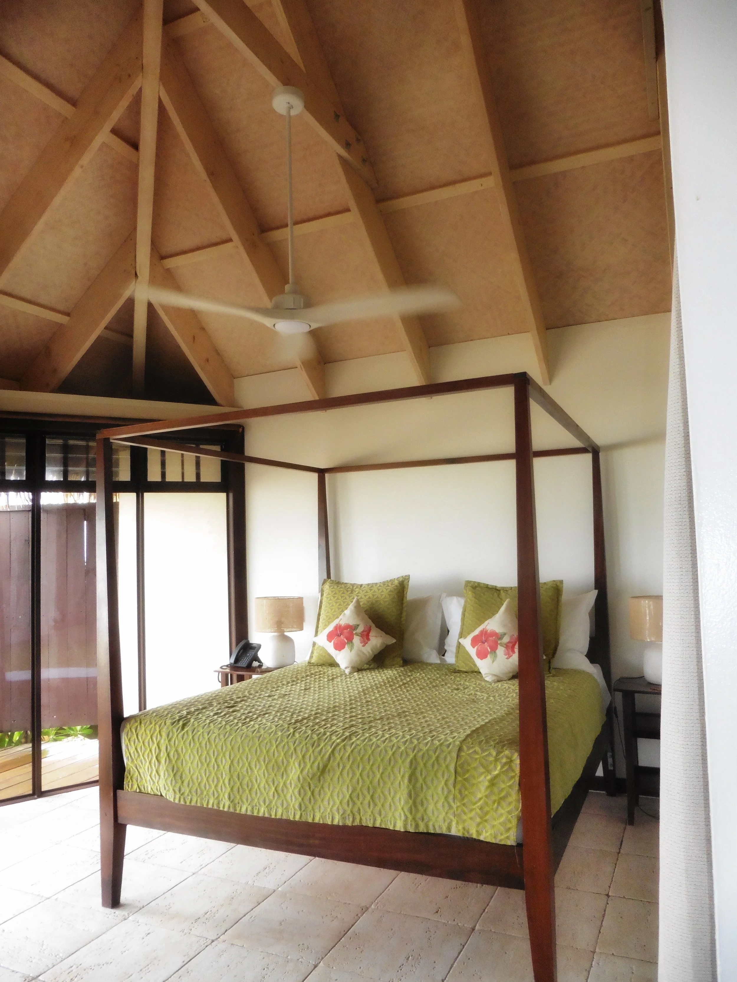 Tropical bedroom with canopy bed and wooden ceilings at Sea Change Villas in Rarotonga