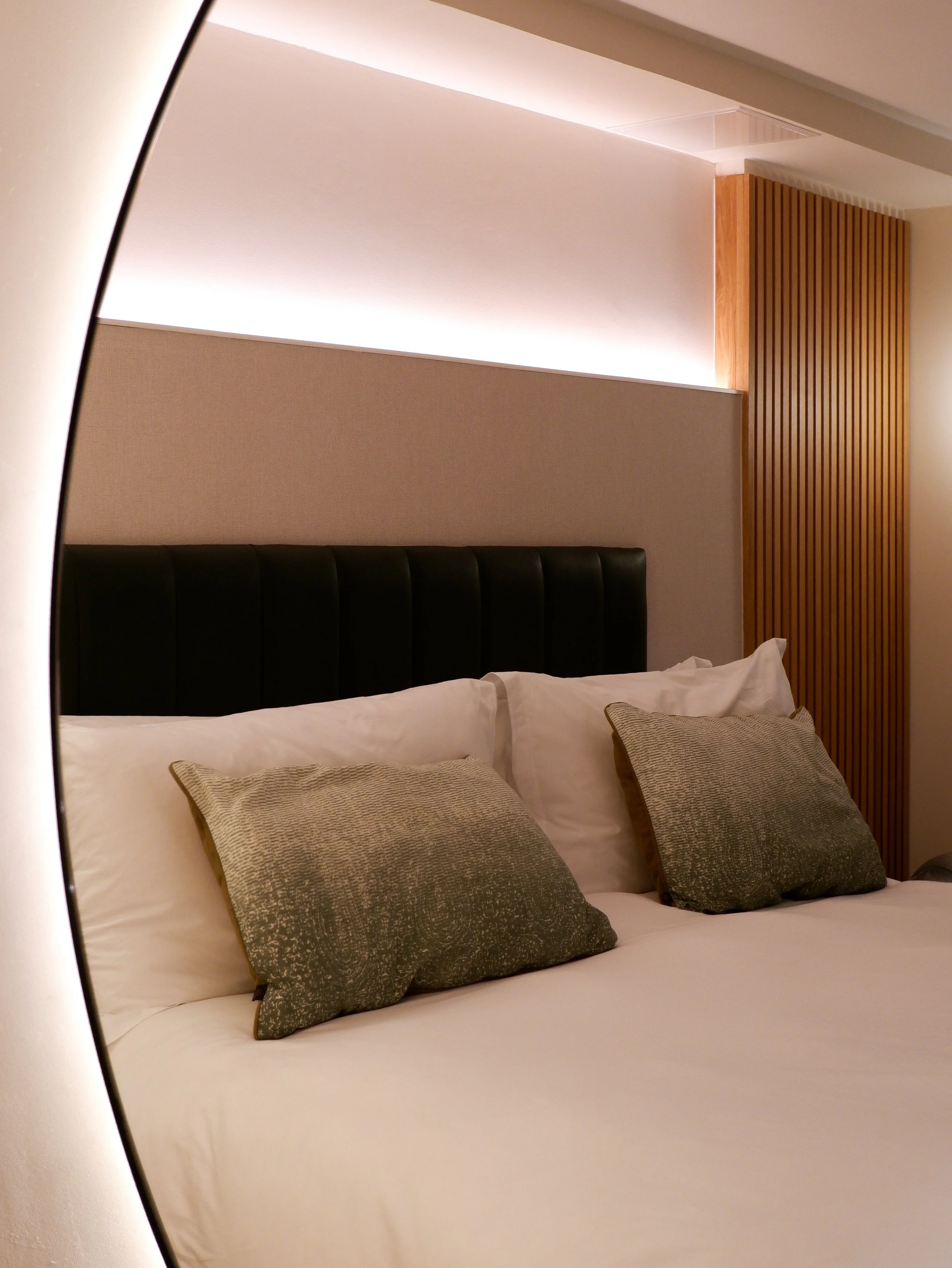 Comfortable hotel bed with crisp white linens, green accent cushions, and a softly illuminated headboard