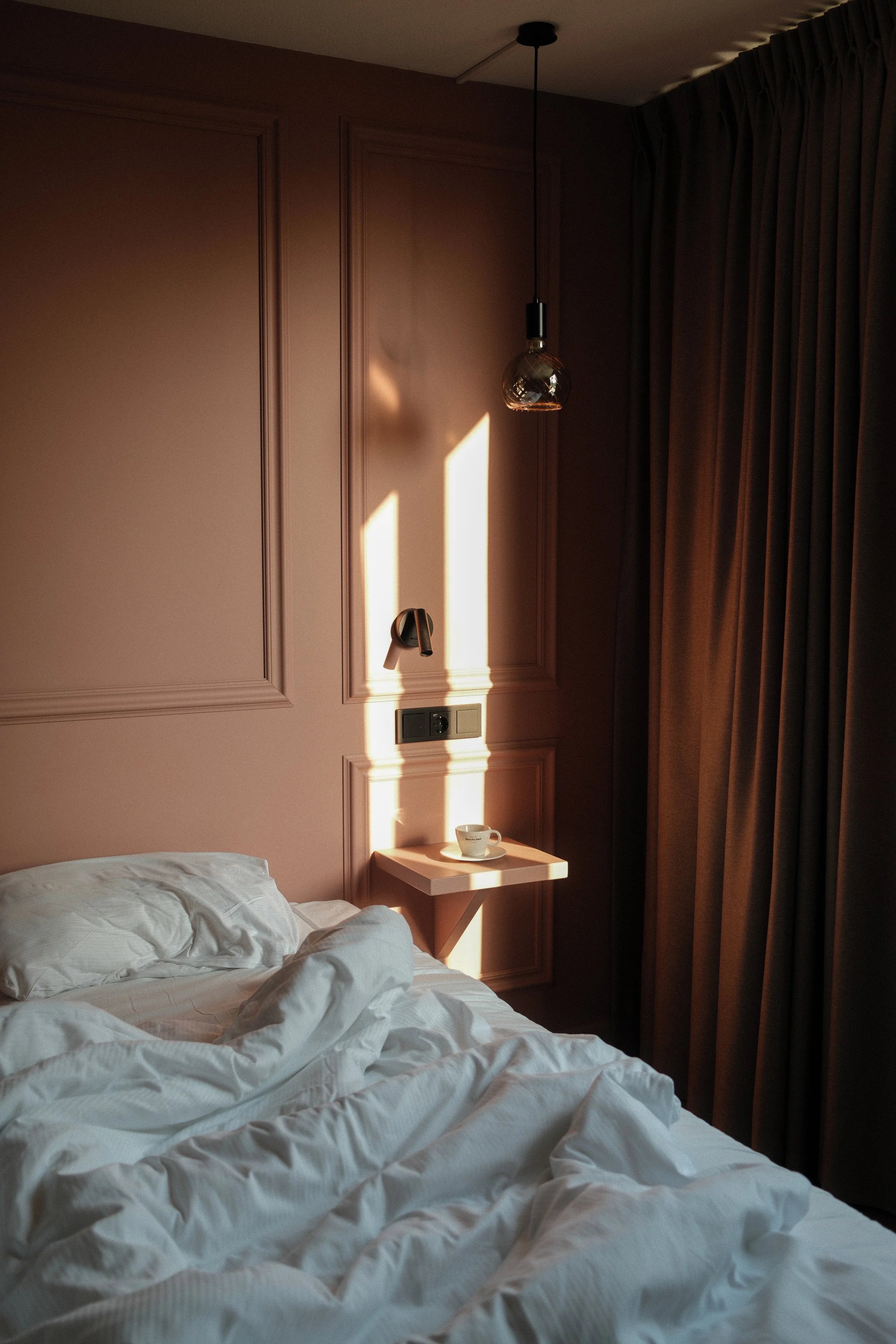 Sunlit bedroom corner with soft linens, warm wall tones, and natural light casting geometric shadows, Château St. Gerlach – Vaeshartelt Maastricht.