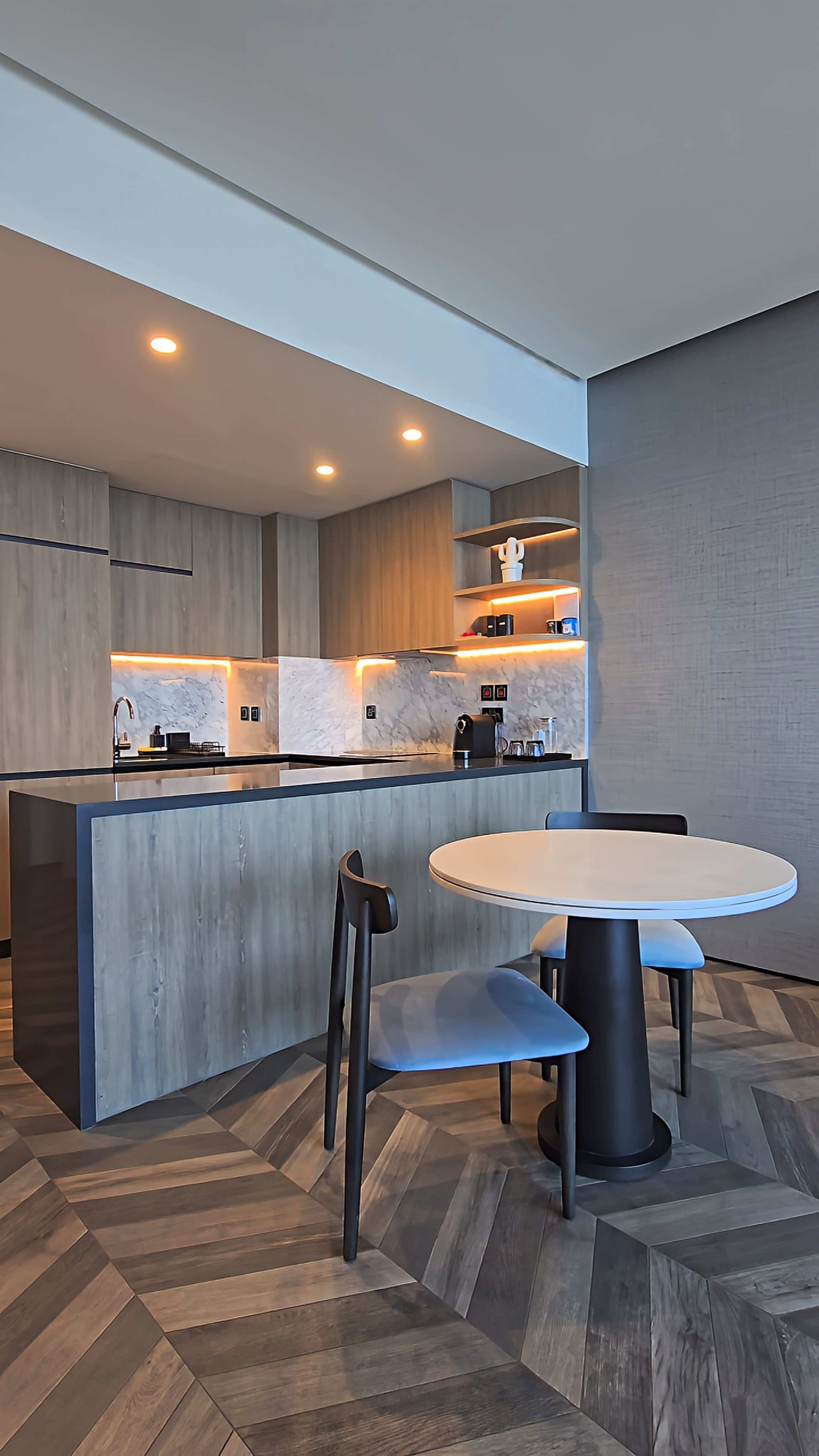 Contemporary suite kitchenette featuring marble countertops, wooden cabinetry, integrated lighting, and a round dining table
