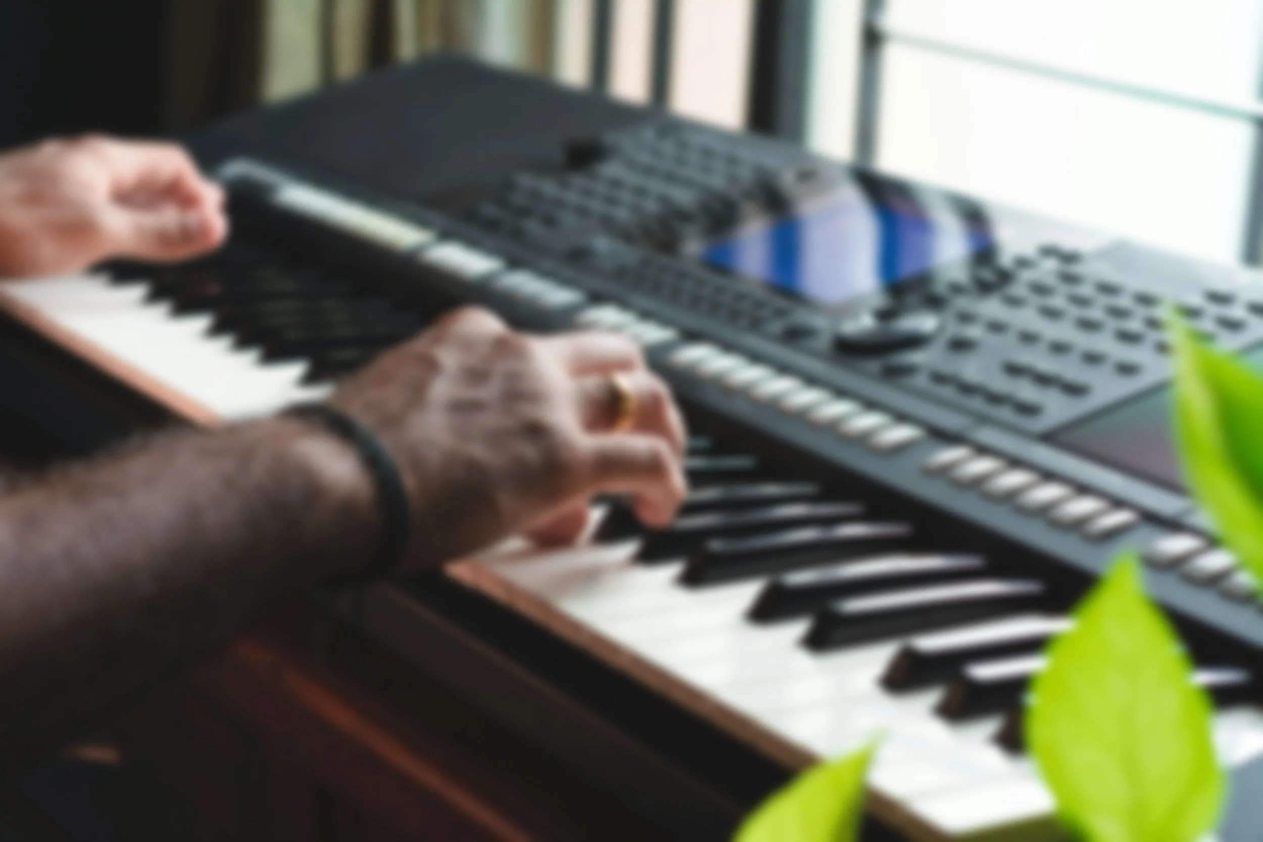 Une personne joue du clavier d'un synthétiseur ou un piano numérique, avec un smartphone posé sur l'instrument et un fond lumineux.