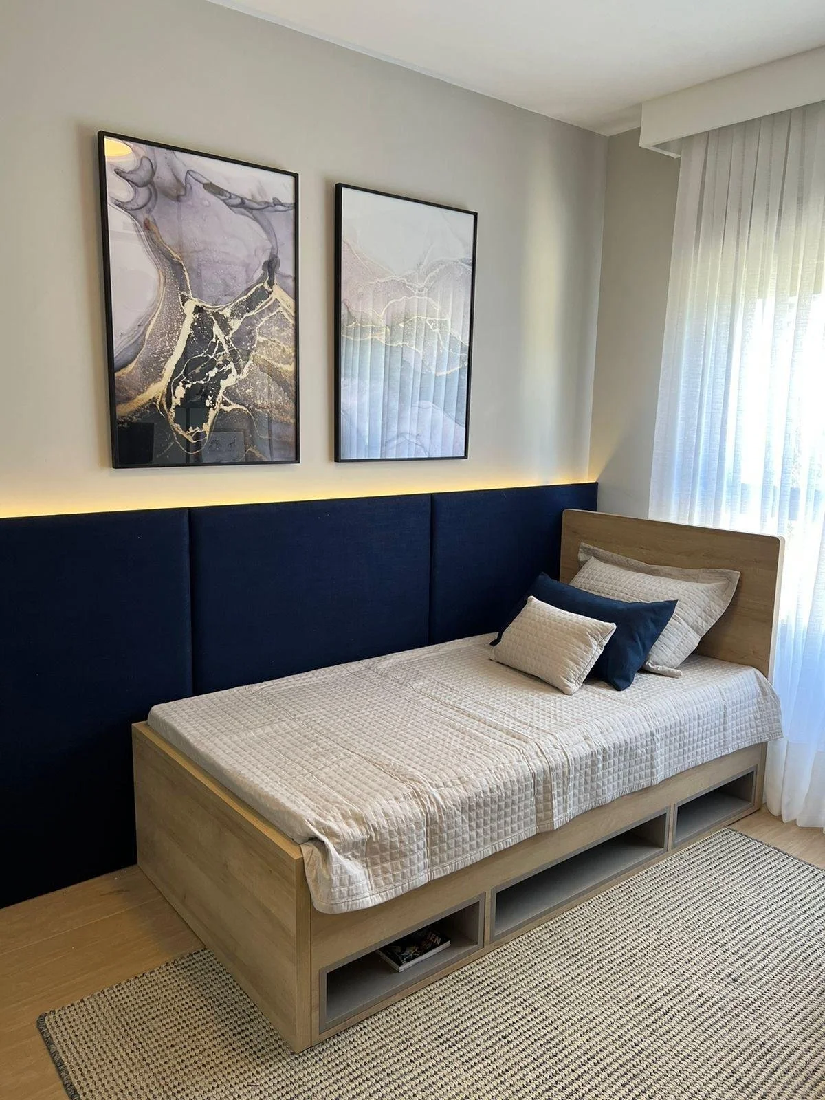 Cameretta da letto 02 in stile minimalista per ragazzo, con testiera in tessuto blu e illuminazione soffusa.