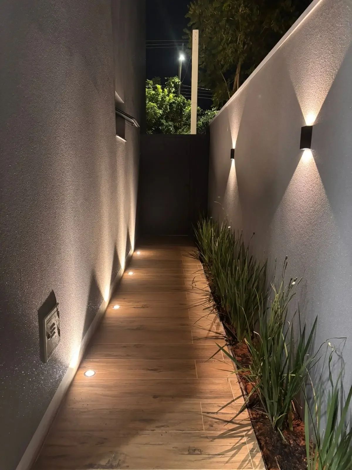 Corridoio ritmato da punti luce puntuali che guidano lo sguardo e il passo. Il cammino prende vita attraverso il gioco di continuità e contrasti tra il gres finto parquet e una fioriera che percorre lateralmente la parete. 