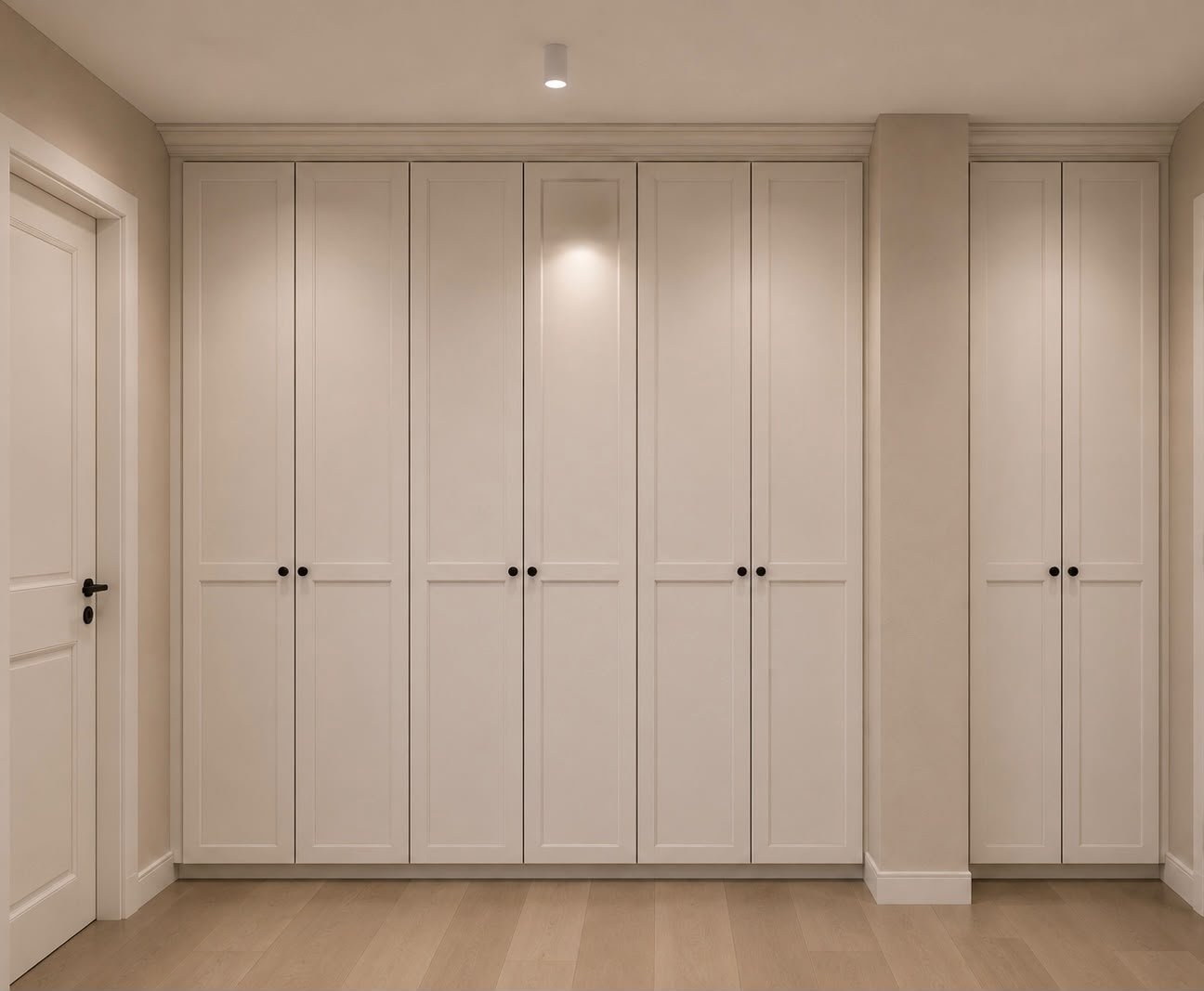 Una grande armadiatura a tutta altezza sfrutta completamente la parete offrendo un'importante capacità contenitiva. Le ante bianche incorniciate si integrano con pareti e porte, rendendo la composizione discreta e architettonica.
