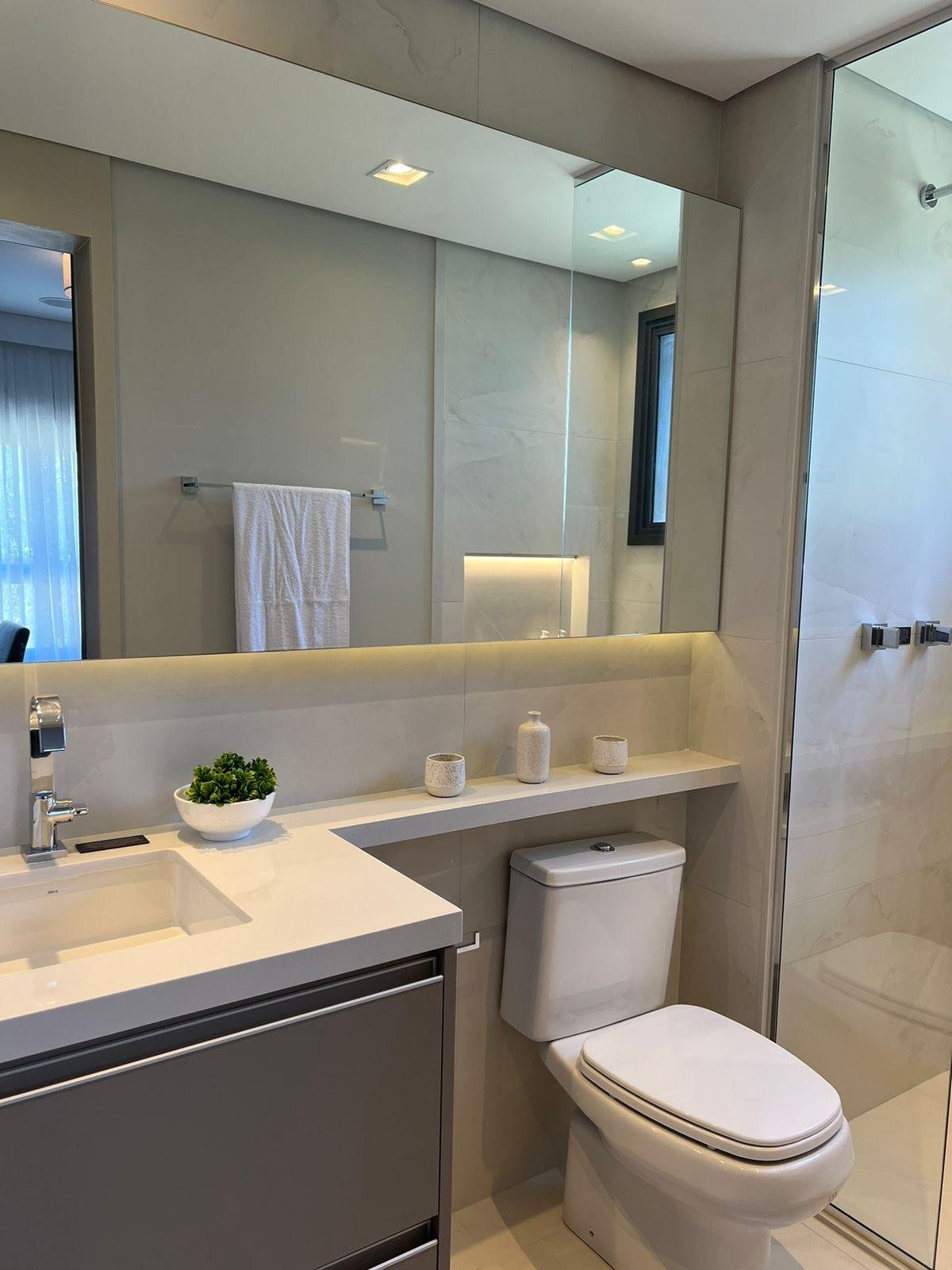 Bagno della stanza 02 con lavabo bianco su piano in marmo, mensola sospesa con decorazioni minimaliste e illuminazione a LED integrata. Pareti in tonalità neutre e sanitari dal design pulito.