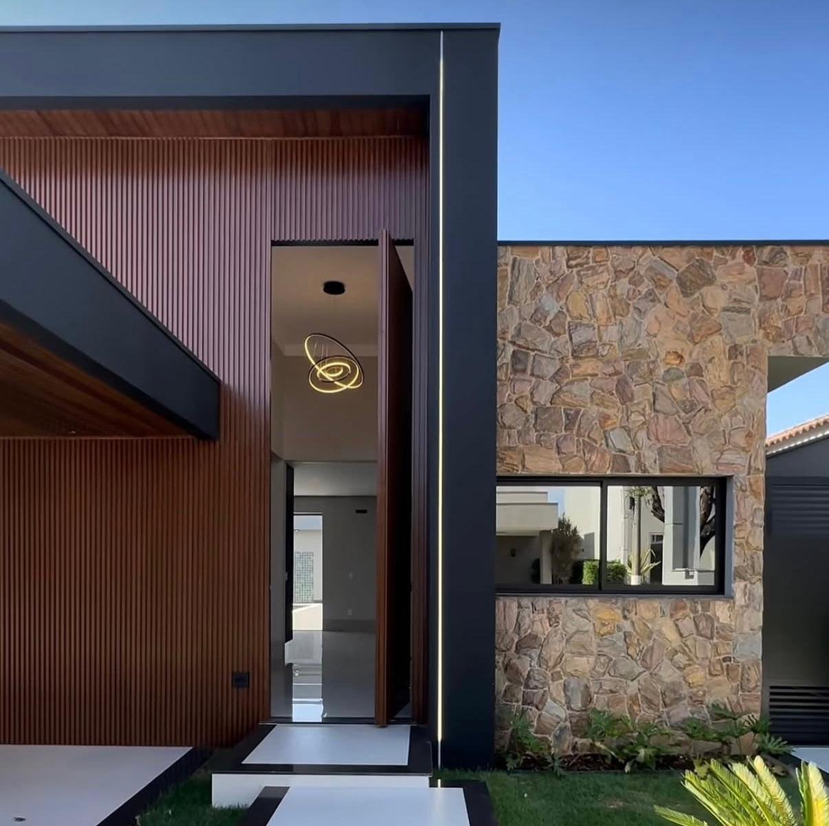 Costruzione ultimata della facciata Villa Esmeralda: pietra naturale, listelli in alluminio e un raggio LED che taglia l'oscurità della facciata nera.