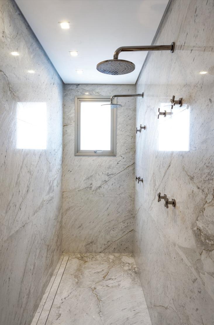 Doccia walk-in rivestita in marmo con soffione a pioggia e rubinetteria a parete.