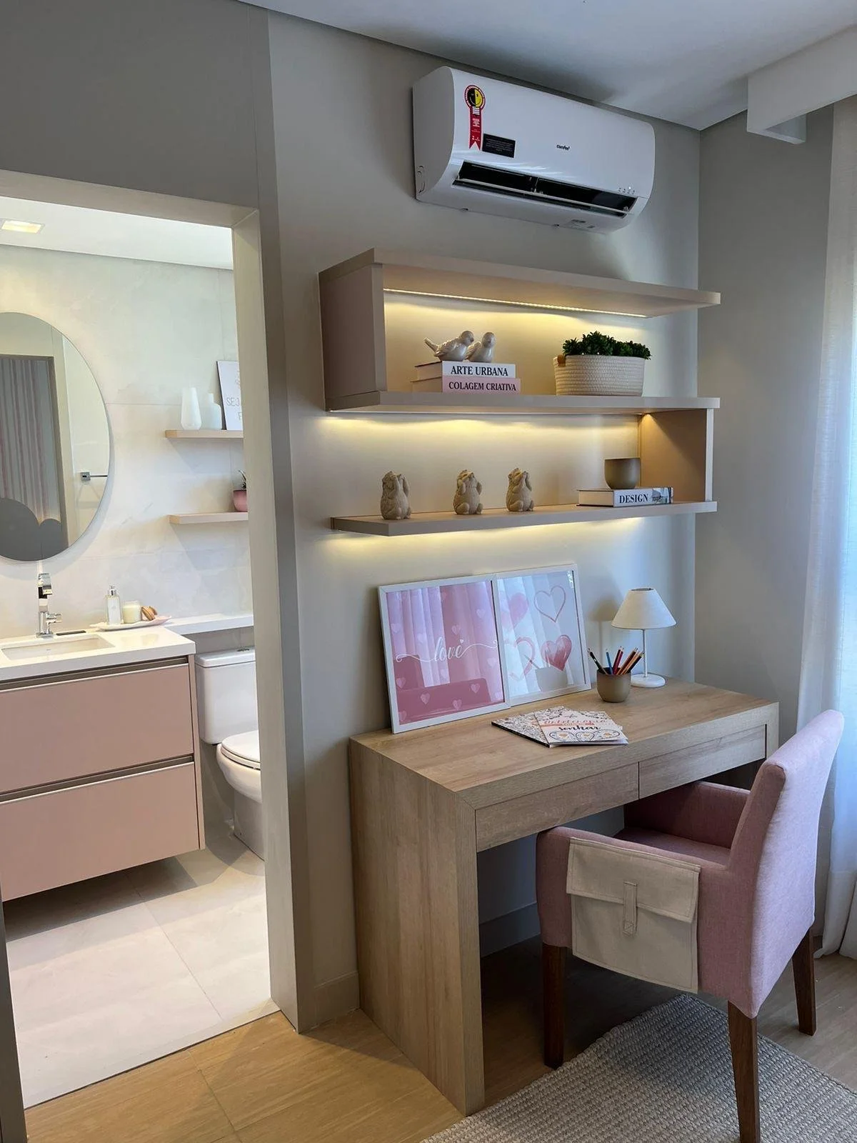 Zona ufficio moderno con scrivania in legno chiaro, sedia rosa e mensole con decorazioni minimaliste. 
