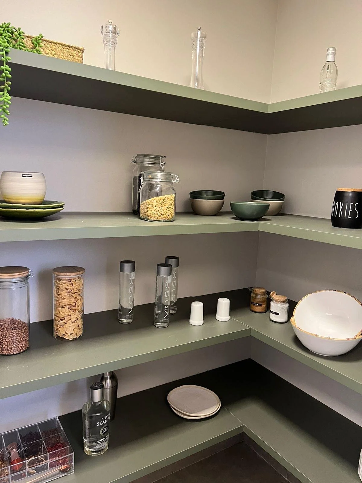 Ripostiglio moderno con scaffali verdi, bottiglie di vetro e contenitori per cereali.