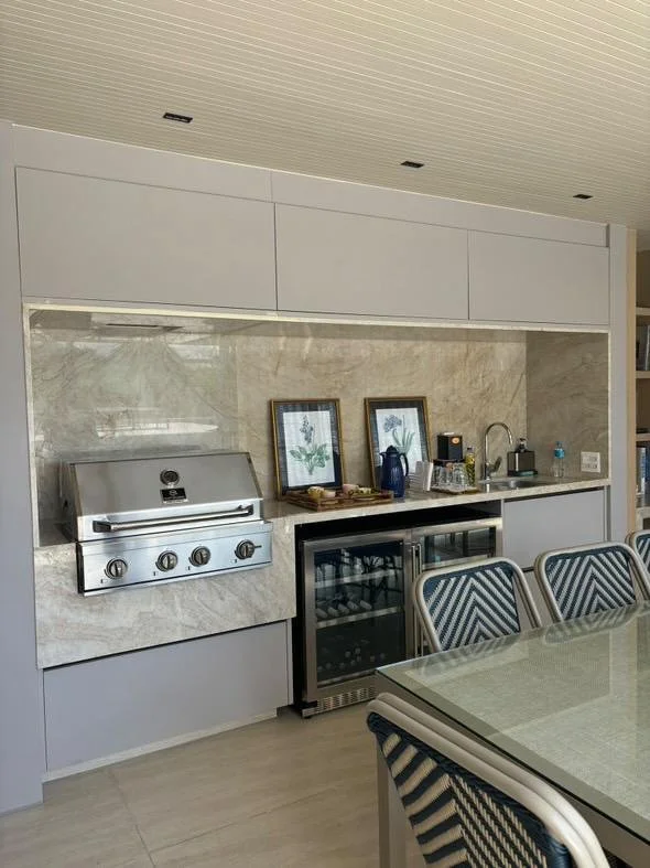 Angolo cucina moderno con arredi su misura: una nicchia in marmo travertino fa da cornice a un piano operativo attrezzato con barbecue professionale e cantinetta per vini.