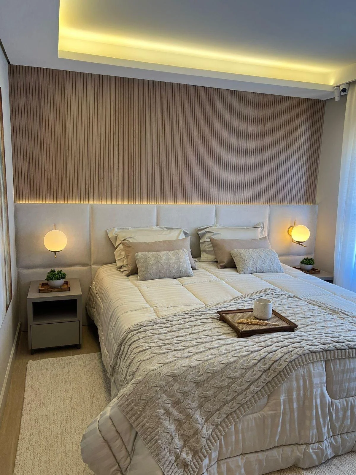 Camera matrimoniale elegante con illuminazione soffusa a LED, testata del letto in tessuto a motivo quadrato e pannello in legno con doghe verticali.