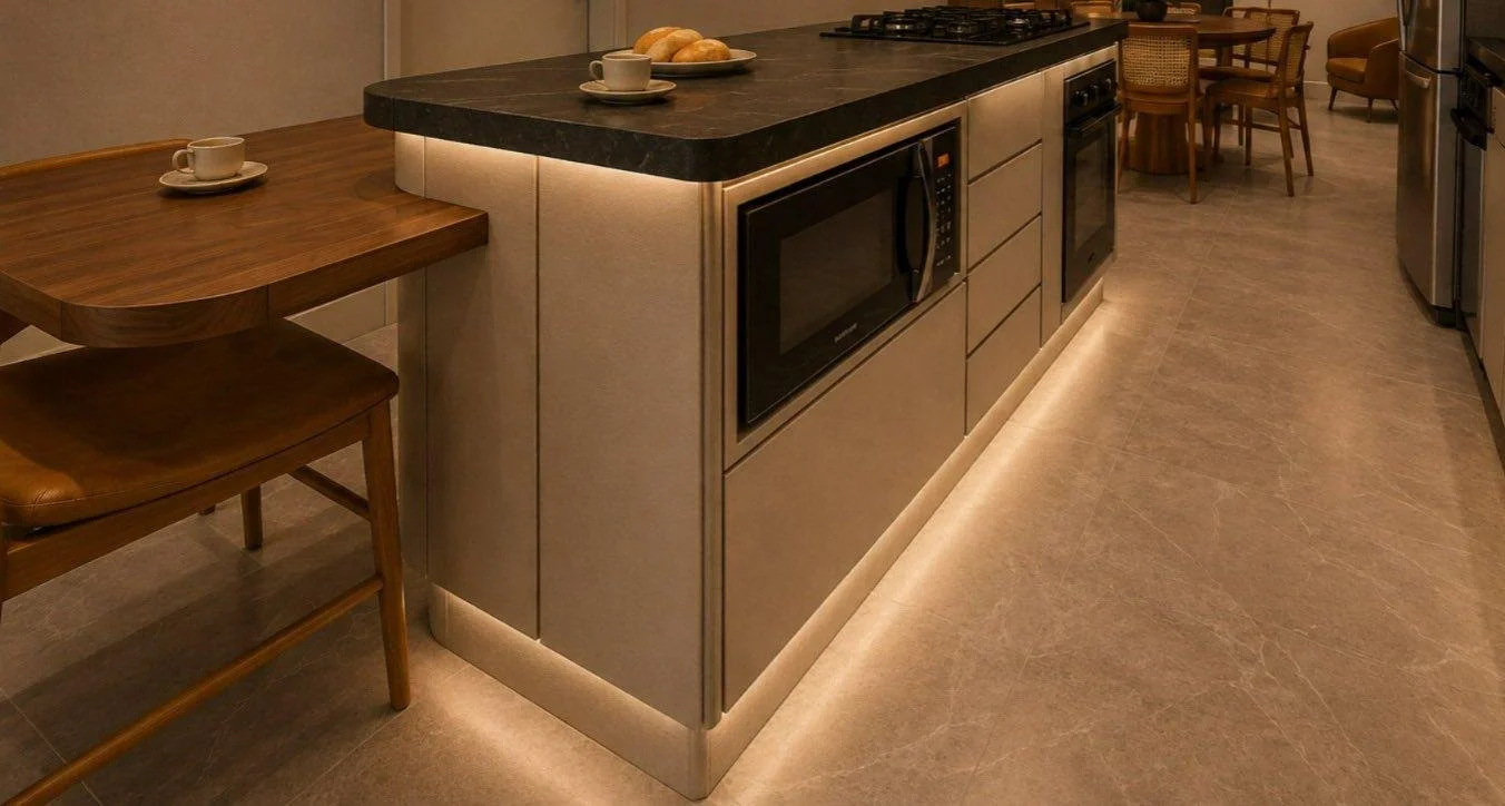 Il piano scuro e il bancone in legno si incontrano nell’isola, con angoli arrotondati e luce integrata alla base.
