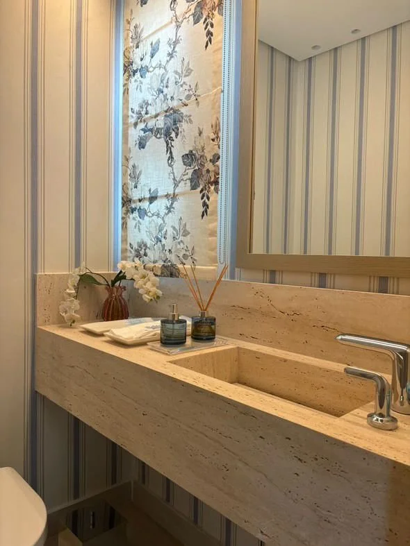 Finestra valorizzata da tenda floreale e palette neutra. Carta da parati a righe verticali, luce lineare a soffitto.