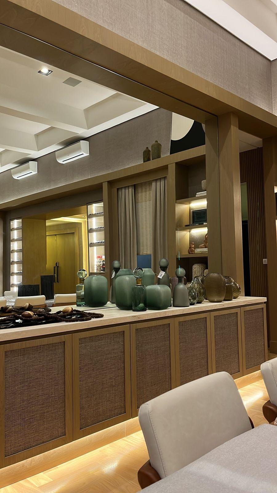 Elegante zona bar con vasi verdi e illuminazione ambientale soffusa. Console in marmo con armadi chiusi ad anta con paglia naturale.