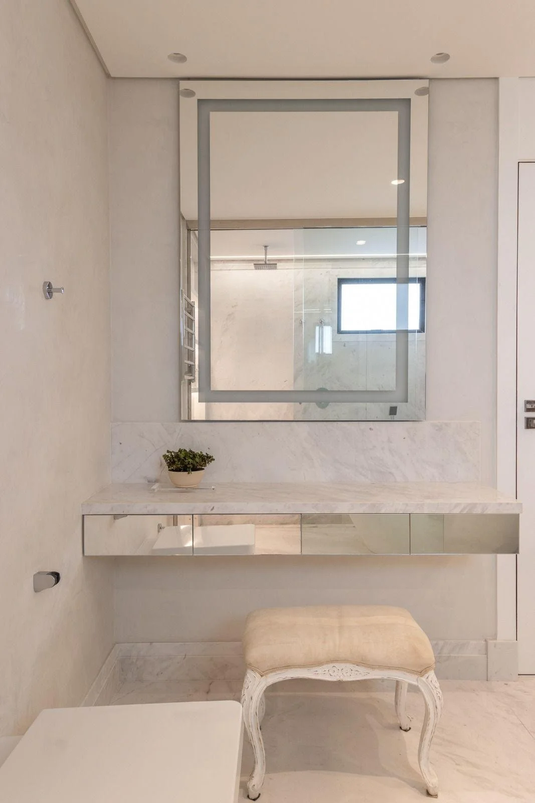 Area trucco del bagno padronale con specchio retroilluminato e poltrona stilo classica.