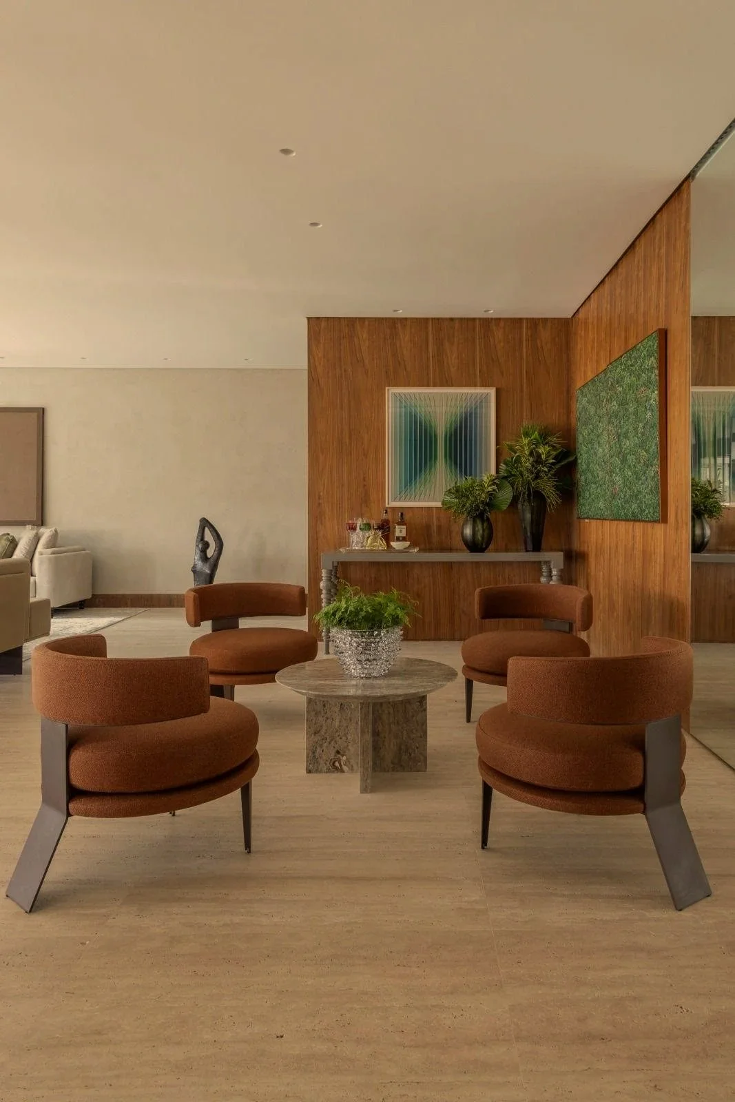 Sala d'attesa con quattro sedie arancioni intorno a un tavolino di pietra, decorato con piante e vasi, con pareti di legno e opere d'arte alle pareti.