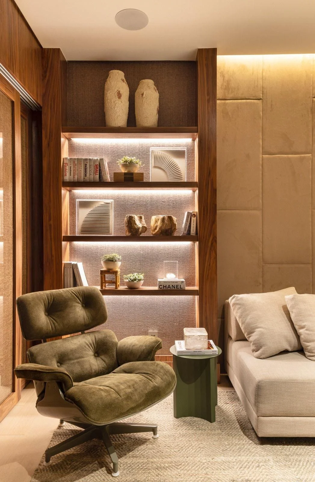 Dettaglio lounge: poltrona iconica e libreria luce calda e mensole decorative illuminate.