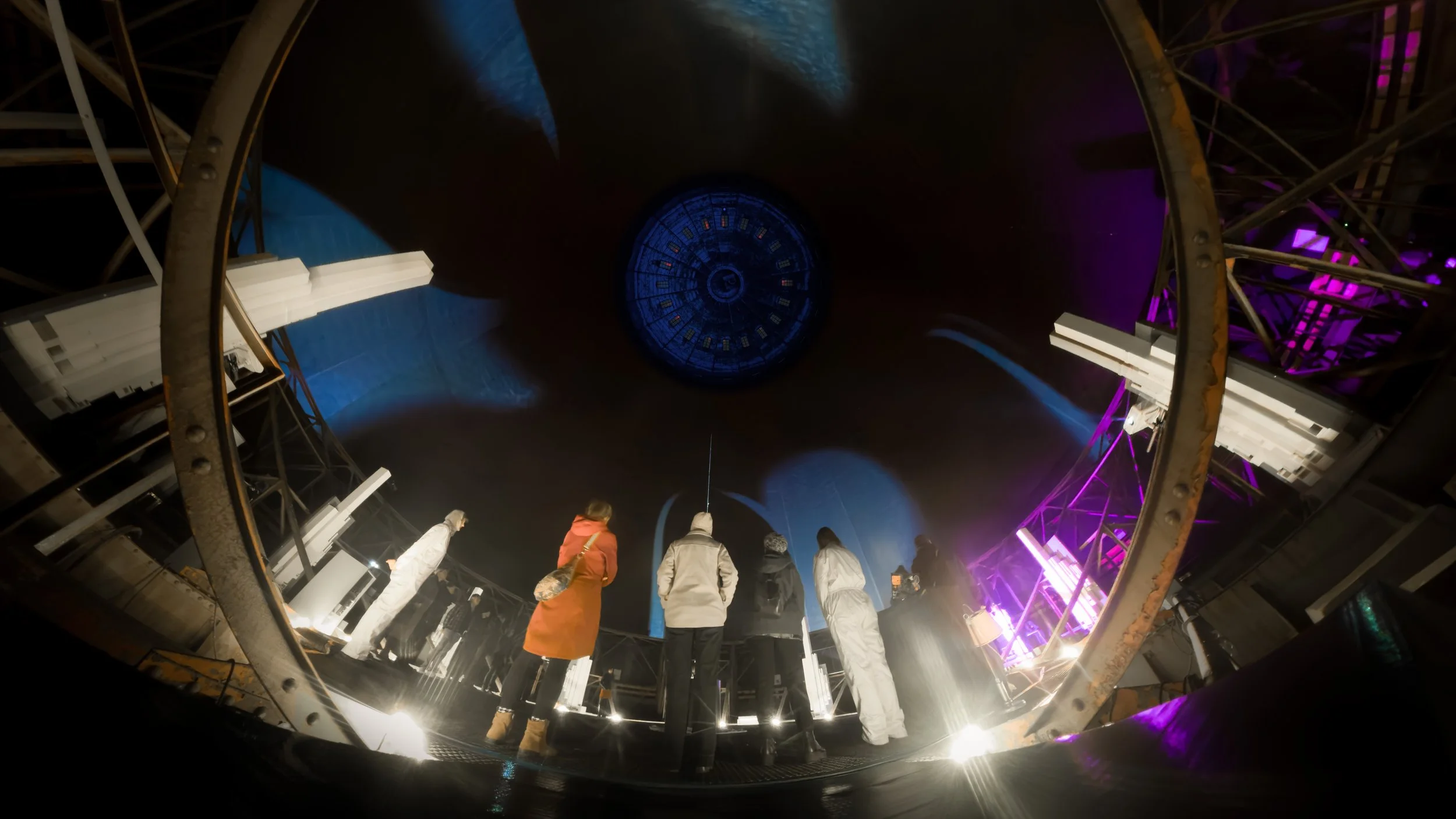 Audience standing inside a large gasometer, looking up at immersive projections and light during a live theatre performance.