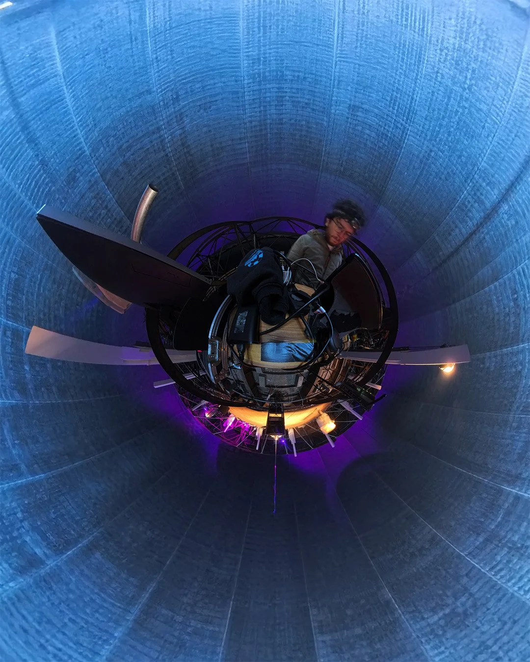 Michael Gamböck standing in a circular room, surrounded by tech equipment, with a fish-eye lens effect creating a spherical view of the scene.