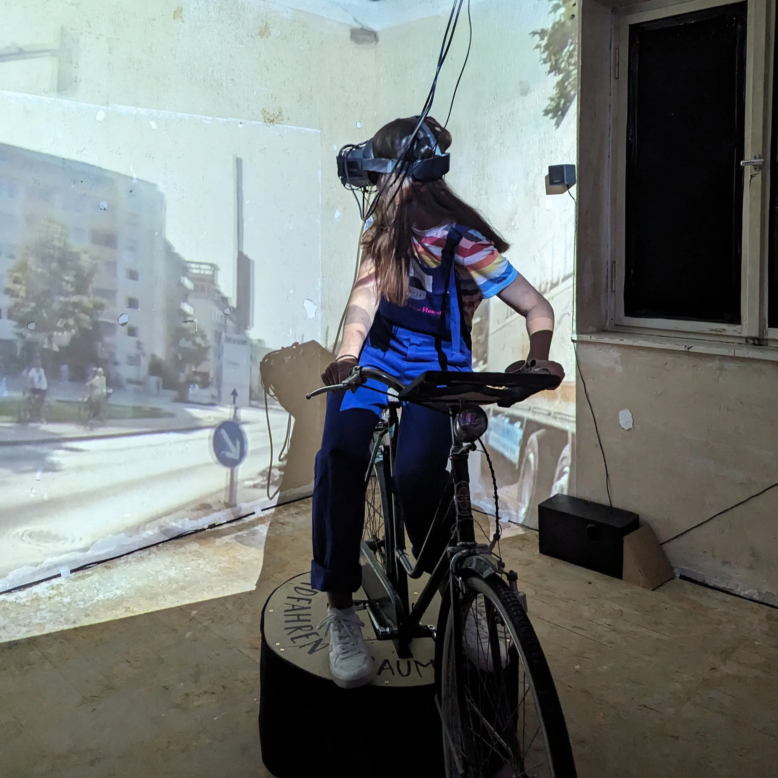 Person riding a bicycle in front of a wall with a projection of an outdoor scene.