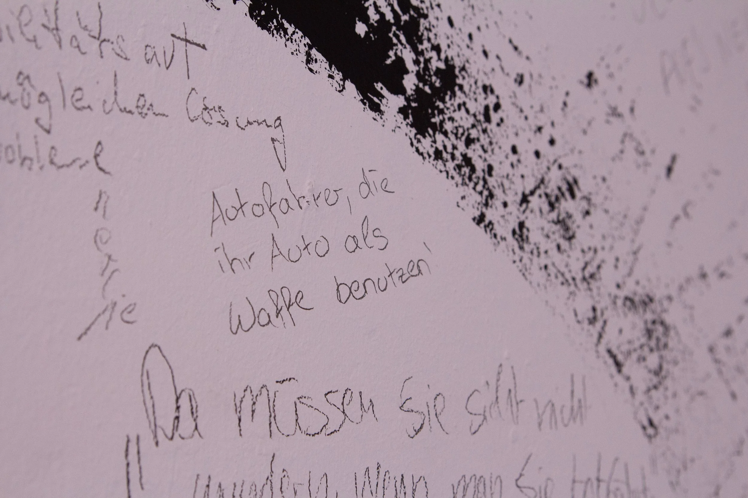 Close-up of handwritten text and black ink splatter on a textured wall.