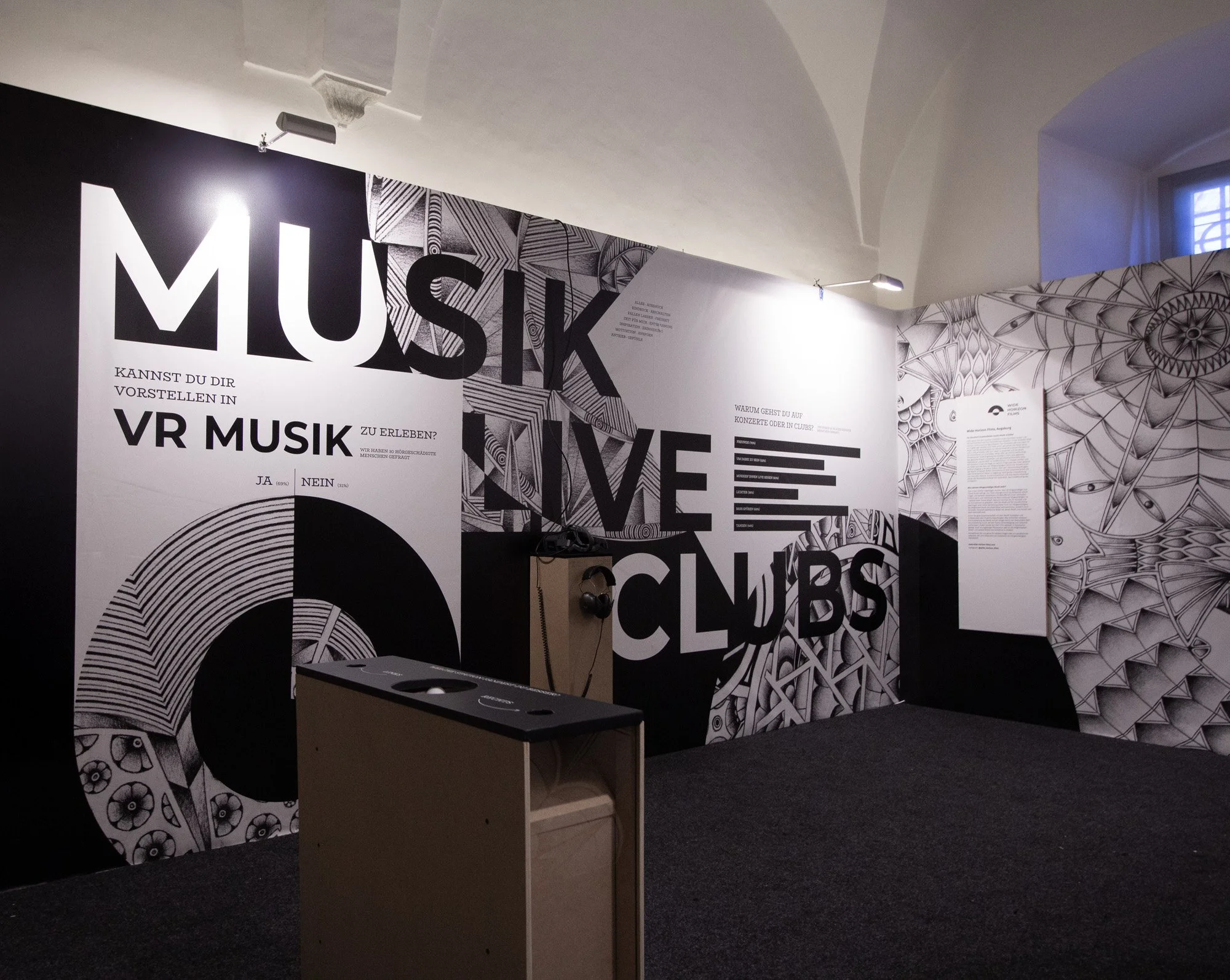Black and white exhibition wall with large text reading 'MUSIK', 'LIVE' and 'CLUBS', featuring geometric and patterned artwork.