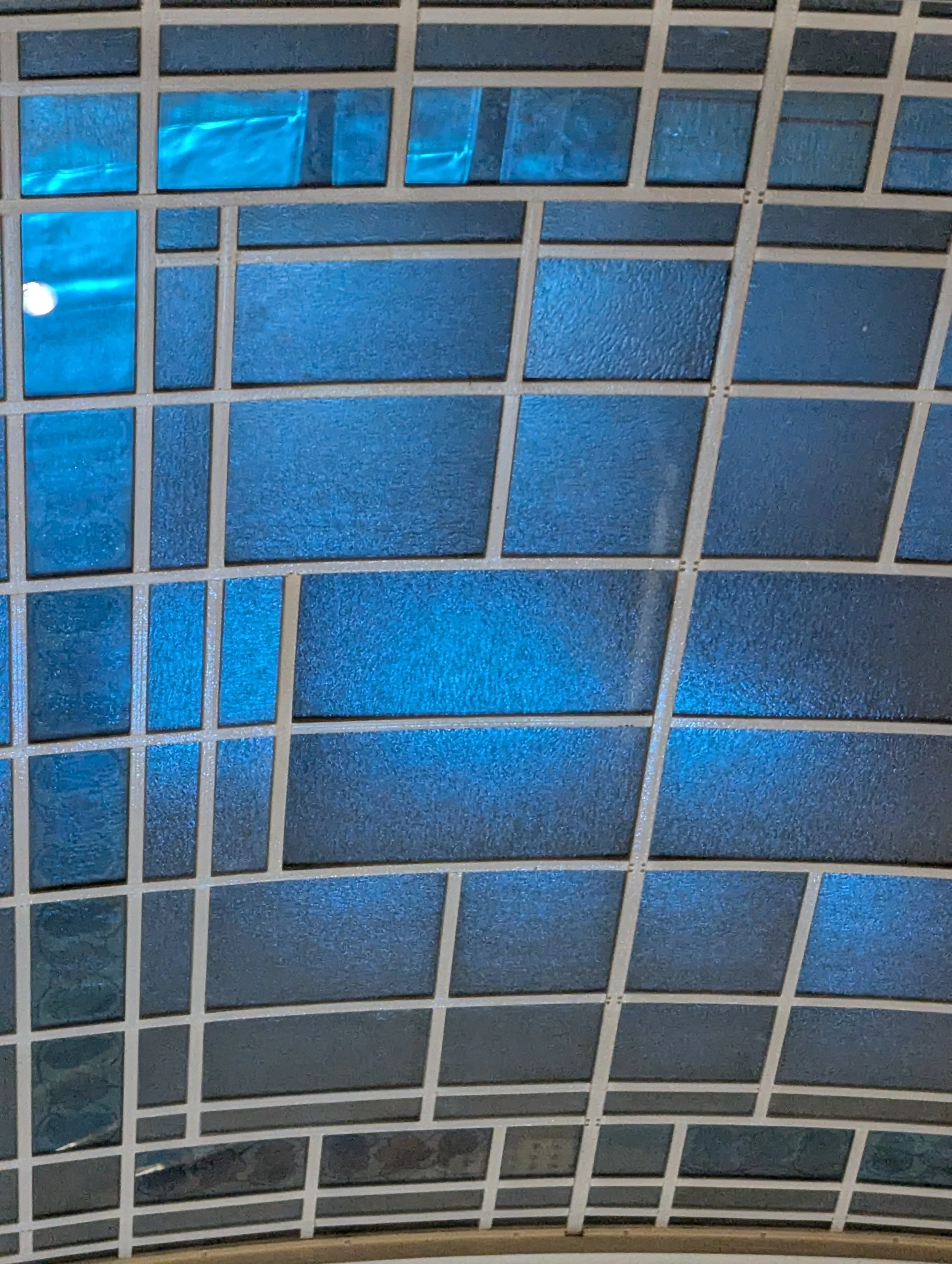 Close-up of a curved ceiling with blue-tinted glass panels and white grout lines.