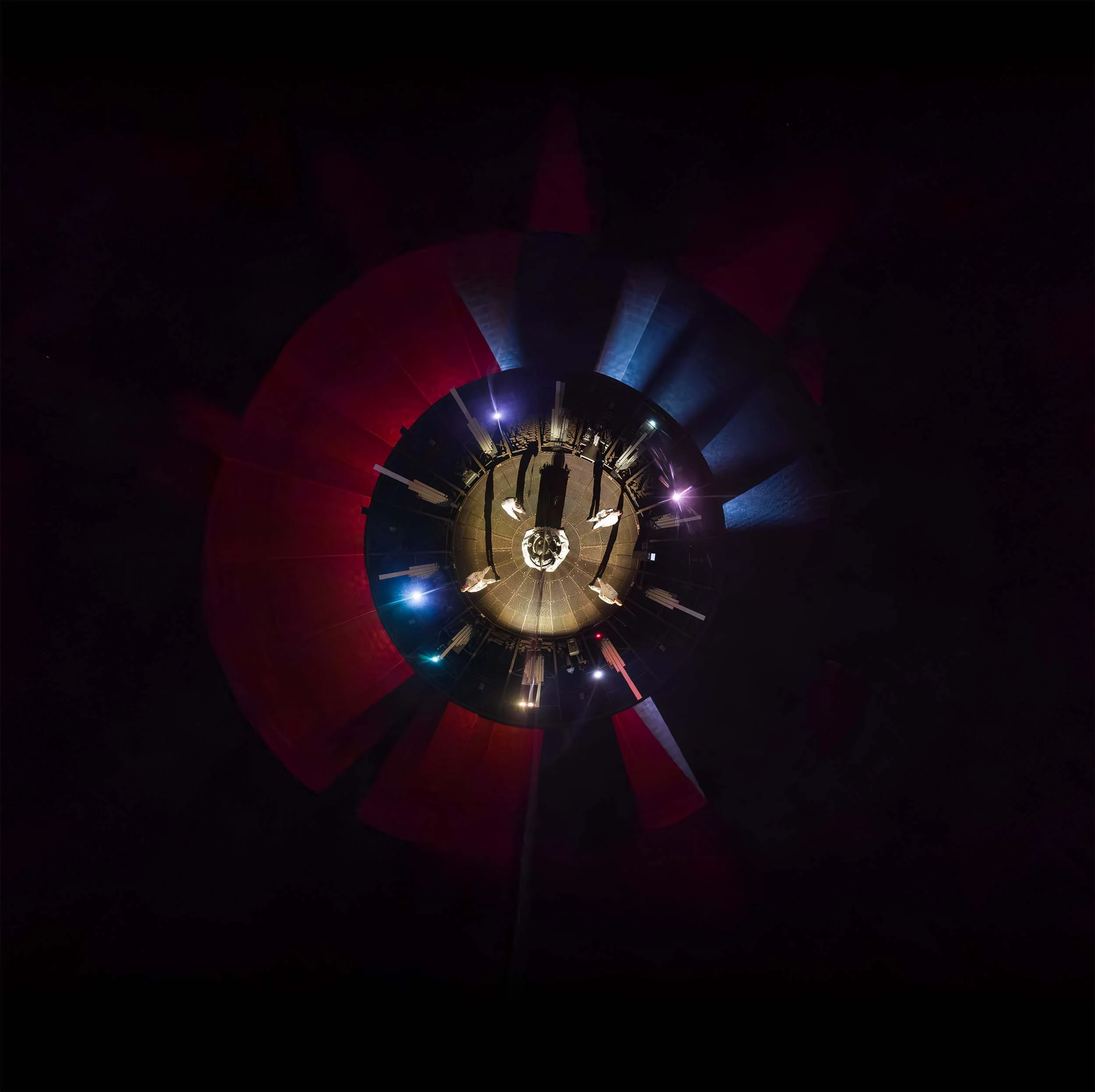 Top view of performers inside a circular gasometer space with immersive red and blue projection lighting.