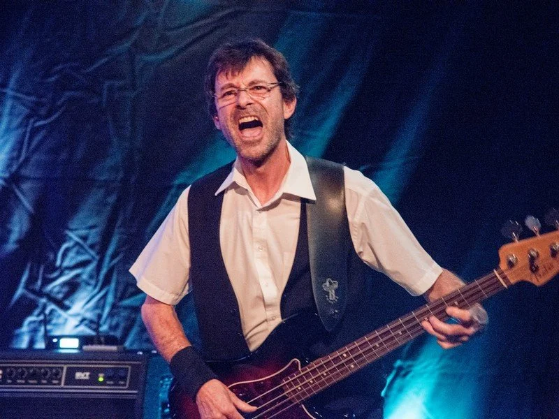 Ein Mann spielt Gitarre und singt leidenschaftlich auf einer Bühne bei einem Live-Konzert.