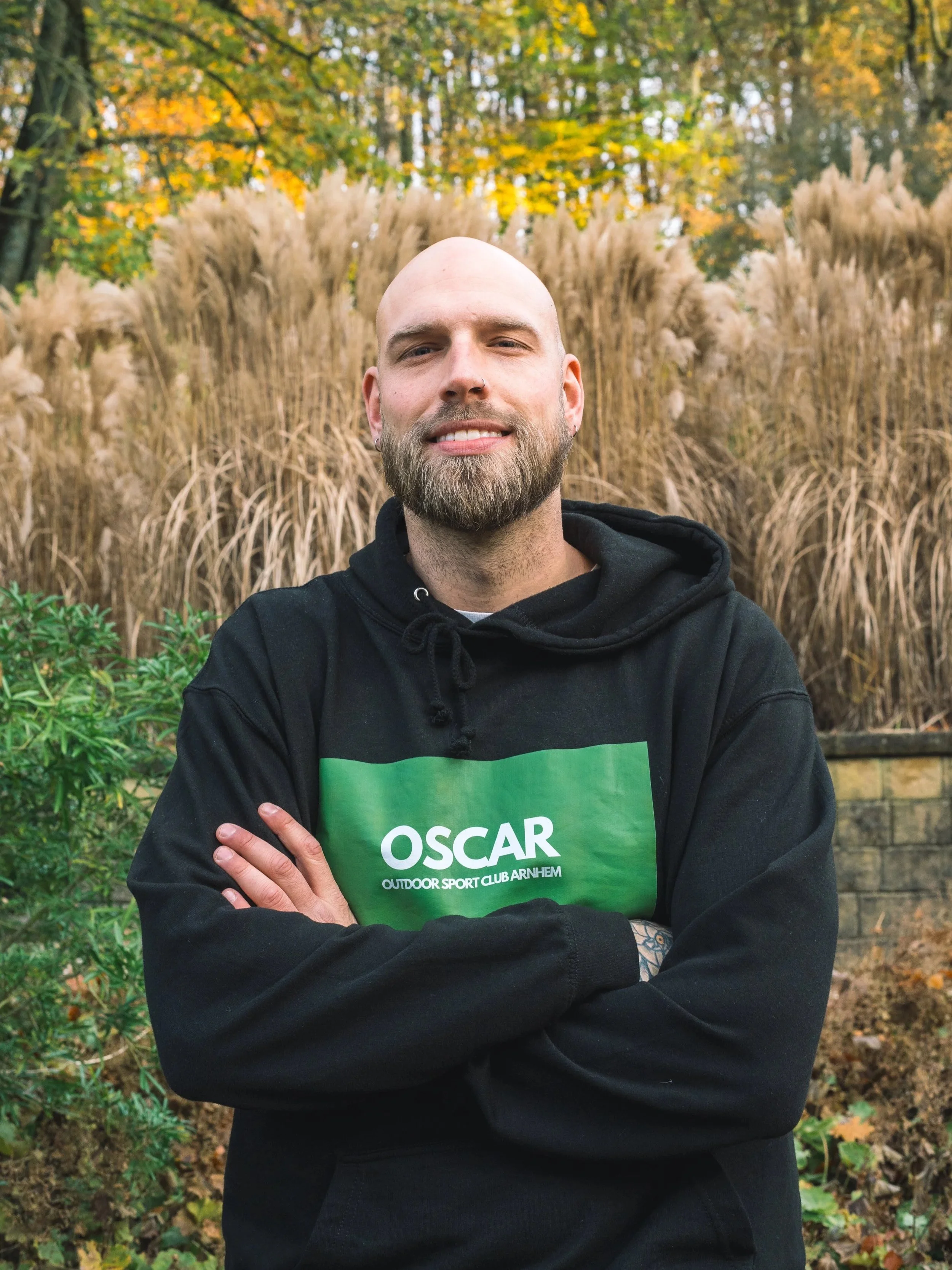 A smiling man with a beard wearing a beanie, white sweater, and dark pants standing outdoors on concrete steps.