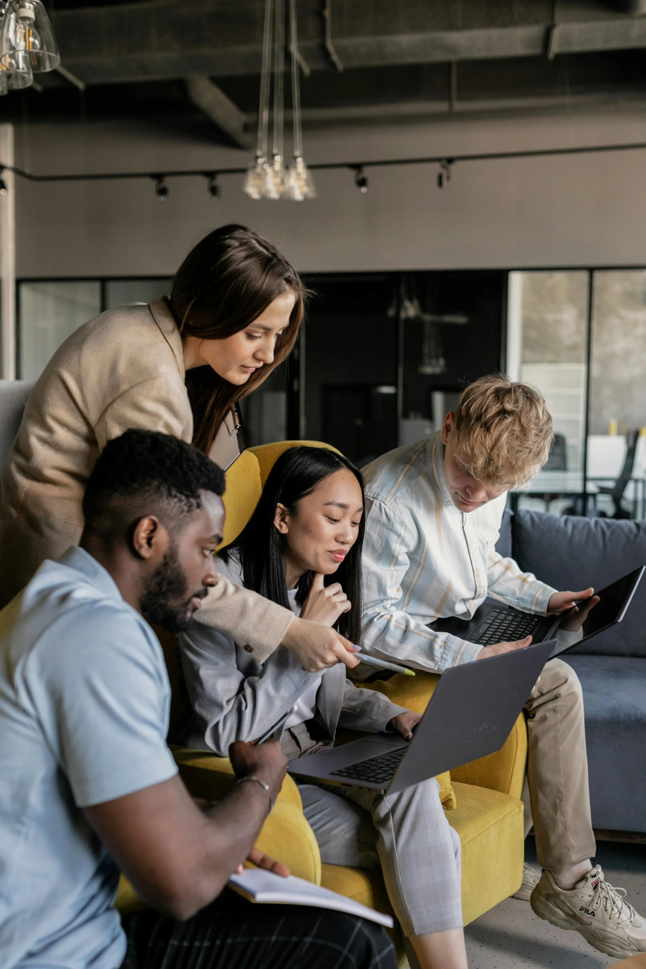 Four young adults working together with laptops and a tablet in a modern, casual office setting.