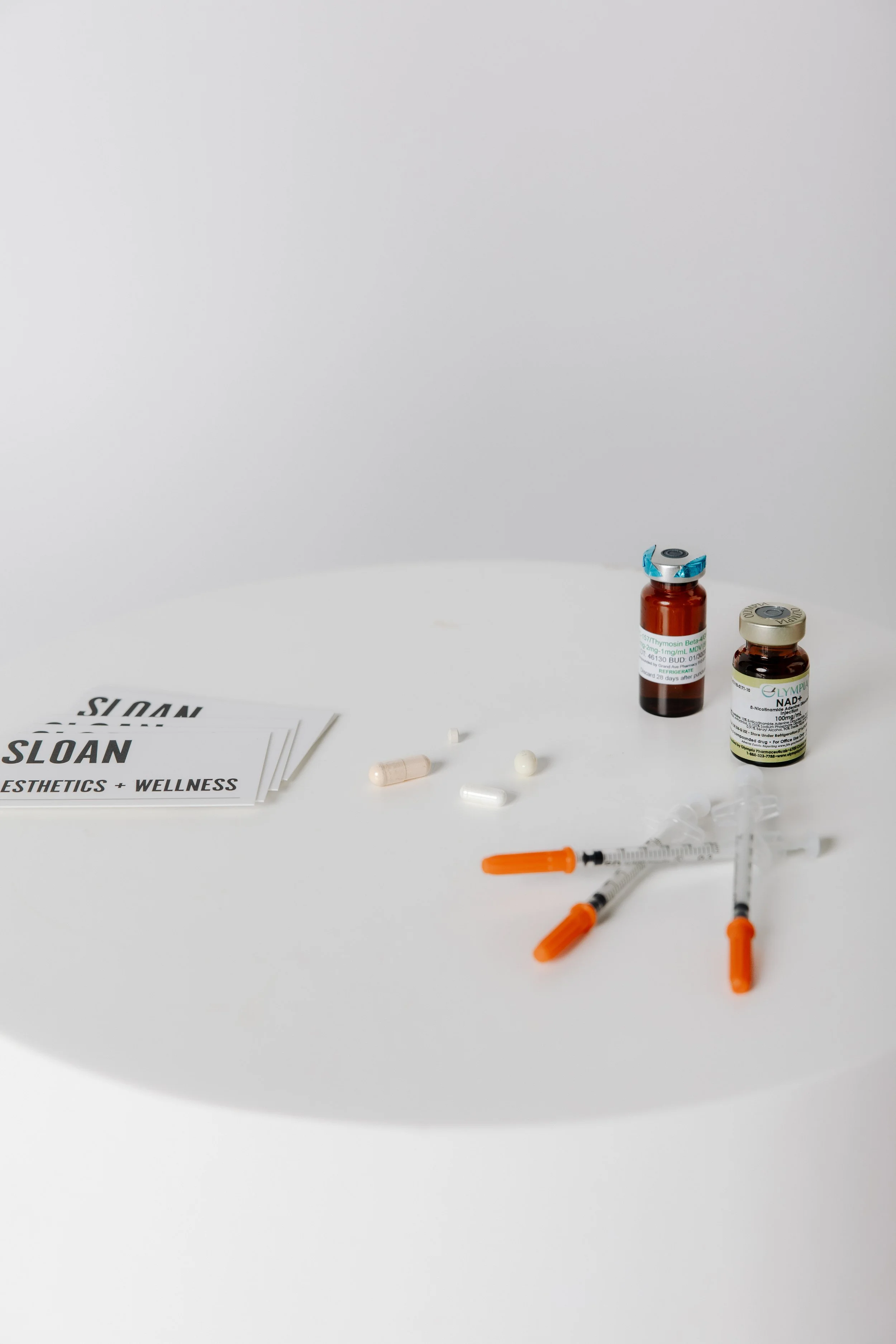 A person about to receive a vaccination shot in their upper arm, with their hand resting on their shoulder. The person is wearing rings, bracelets, and has manicured nails, and is dressed in a black short-sleeved shirt.