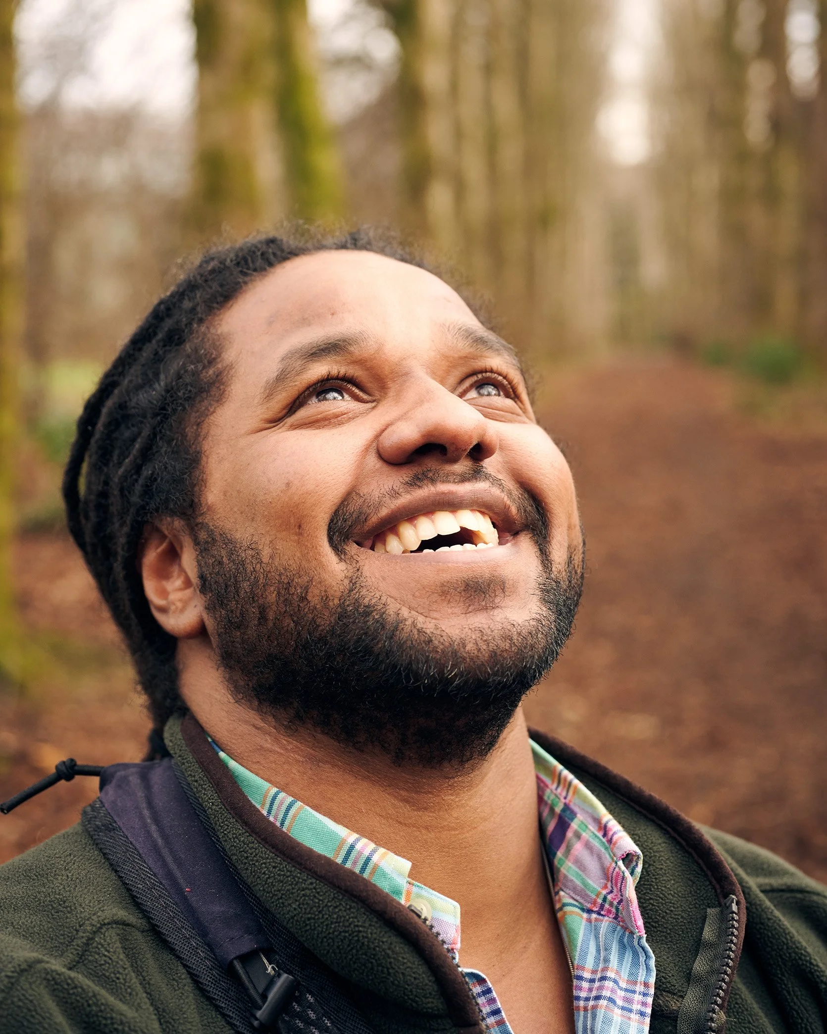 Ranger Hamza from CBBC and Strictly Come Dancing stands in a woodland,  looking up passed the camera and smiling.