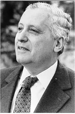 Black and white photo of a man in a suit and tie, looking to the side outdoors.