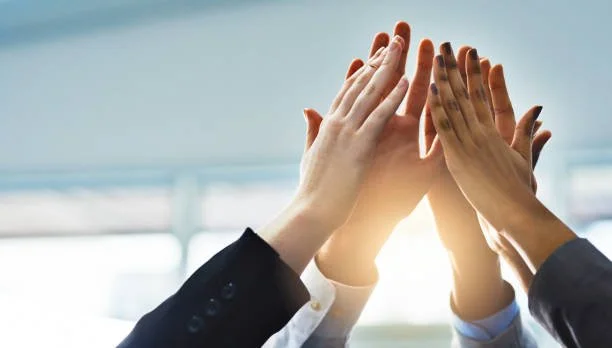 Group of diverse people's hands high-fiving in a bright office setting.