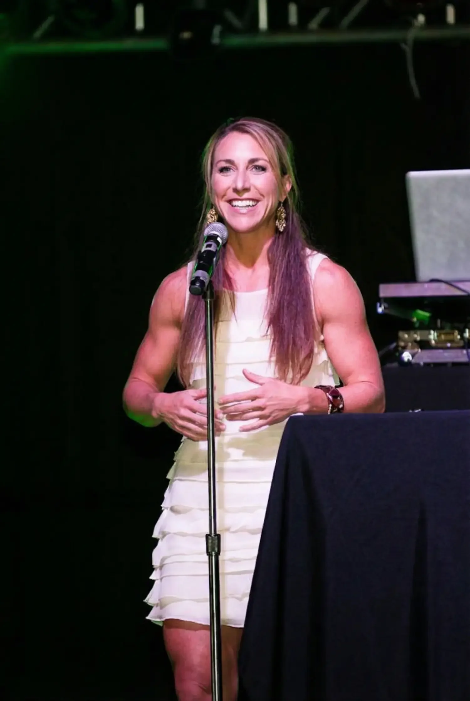 Lisa Fierer speaking on stage at a live event, standing at a microphone and smiling.