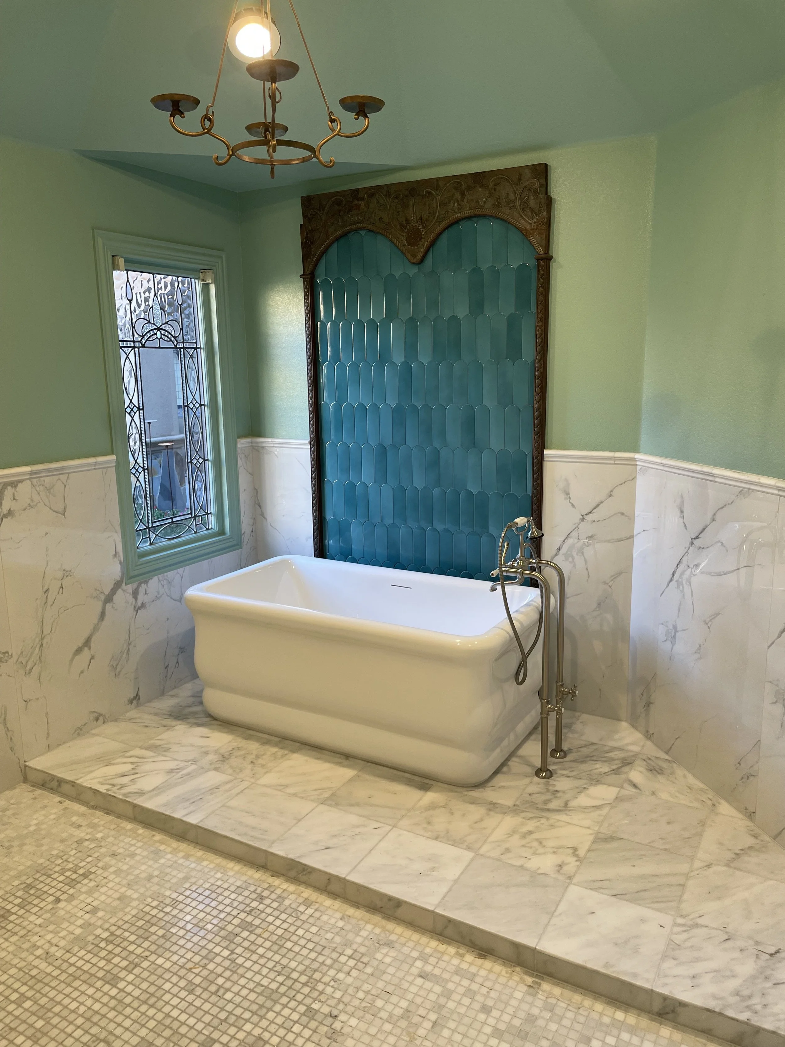 Freestanding tub on white marble tile with green accent tile.