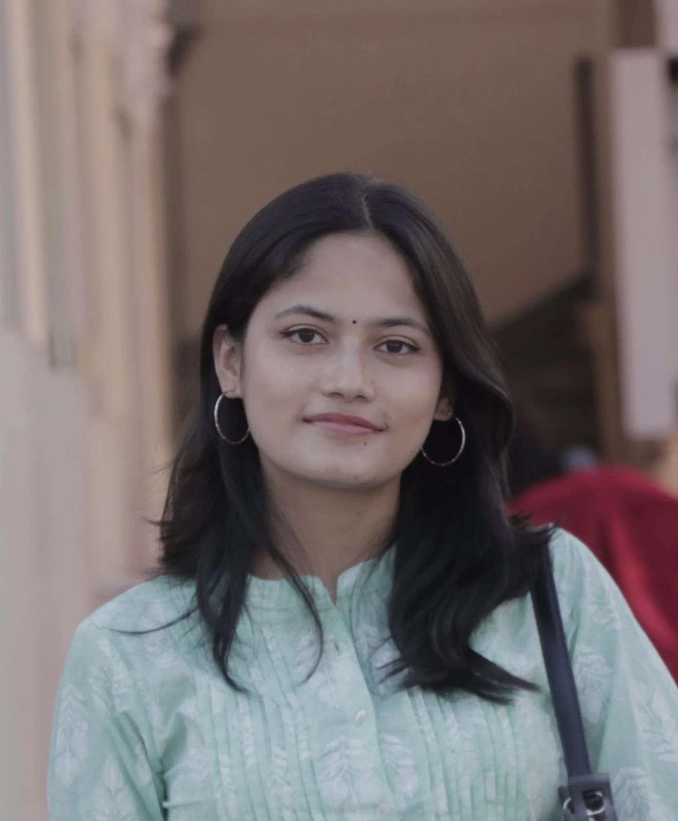 A young woman with long black hair, wearing hoop earrings and a light green traditional Indian kurta, standing outdoors.