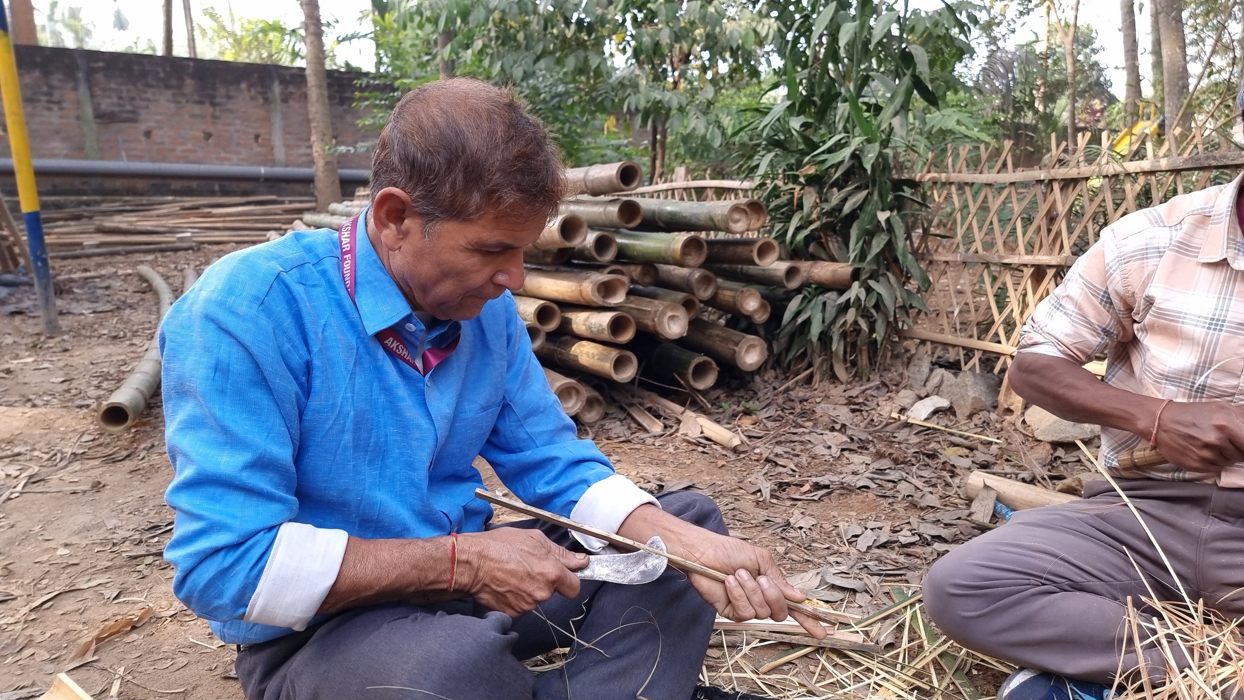 Smiling woman with black hair in a blue top, surrounded by green plants.