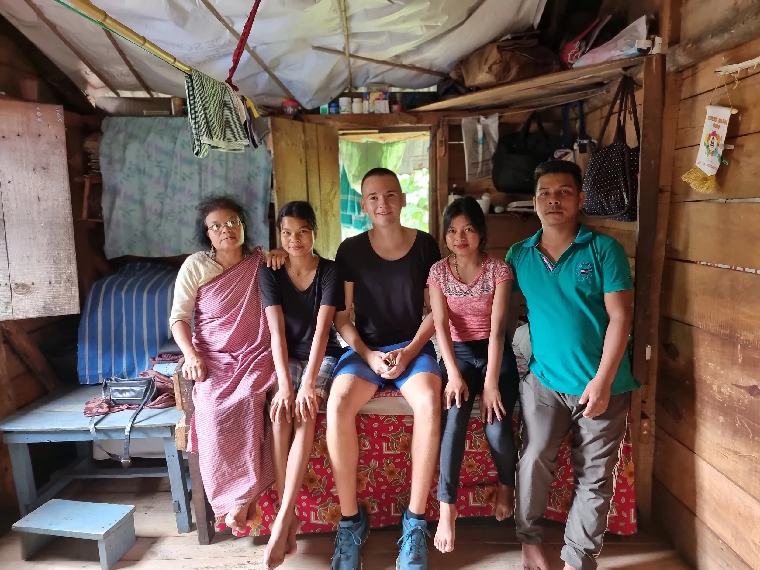 Five people sitting on a bench inside a wooden house, smiling at the camera.
